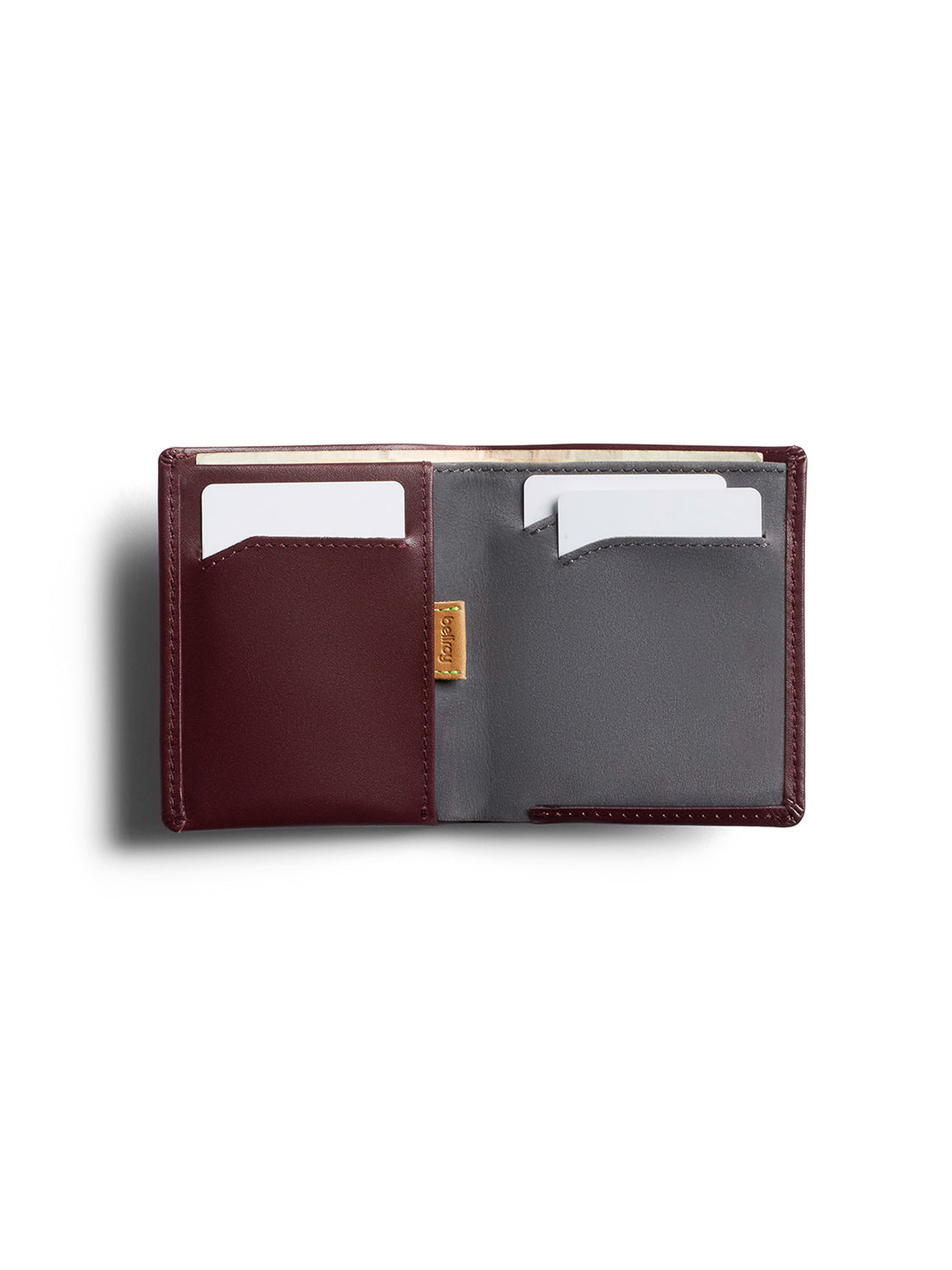 The Bellroy Note Sleeve Wallet is a slim, RFID-protected billfold with two card slots—burgundy (left) and gray (right), each holding a white card. A small gold label sits at the center fold, making it perfect for travel.