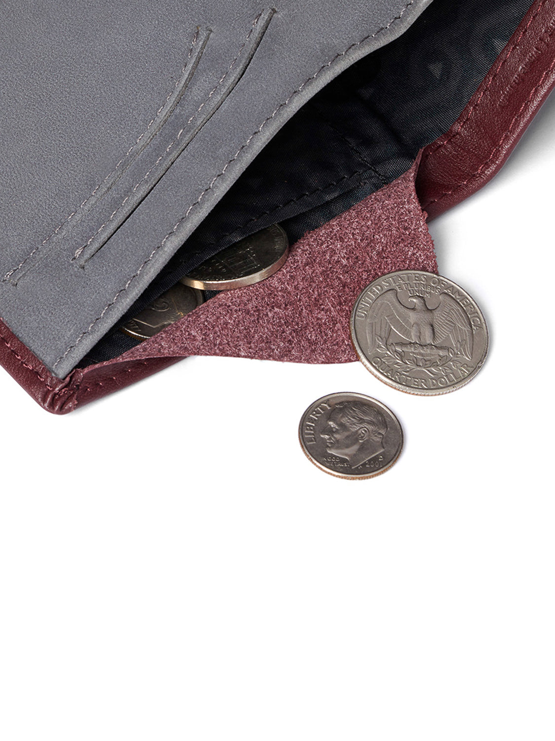 A close-up of the Bellroy Note Sleeve Wallet in gray and maroon, slightly open to reveal several coins inside, with two coins placed on the white surface next to it.