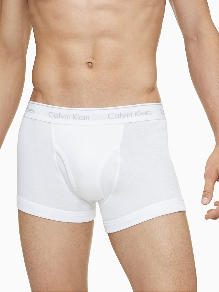 A man is wearing Calvin Klein NB4002 3-Pack Cotton Classic Fit Trunk underwear. The image shows only his torso and upper thighs, with the brand name visible on the waistband.