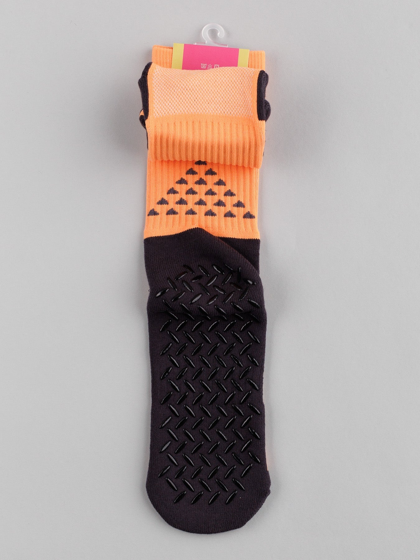 The ID Menswear Grip Sports Socks, in orange and black, feature an anti-slip design with sole patterns and a black triangle folded cuff. The packaging peeks at the top, offering performance and comfort against a plain gray background.