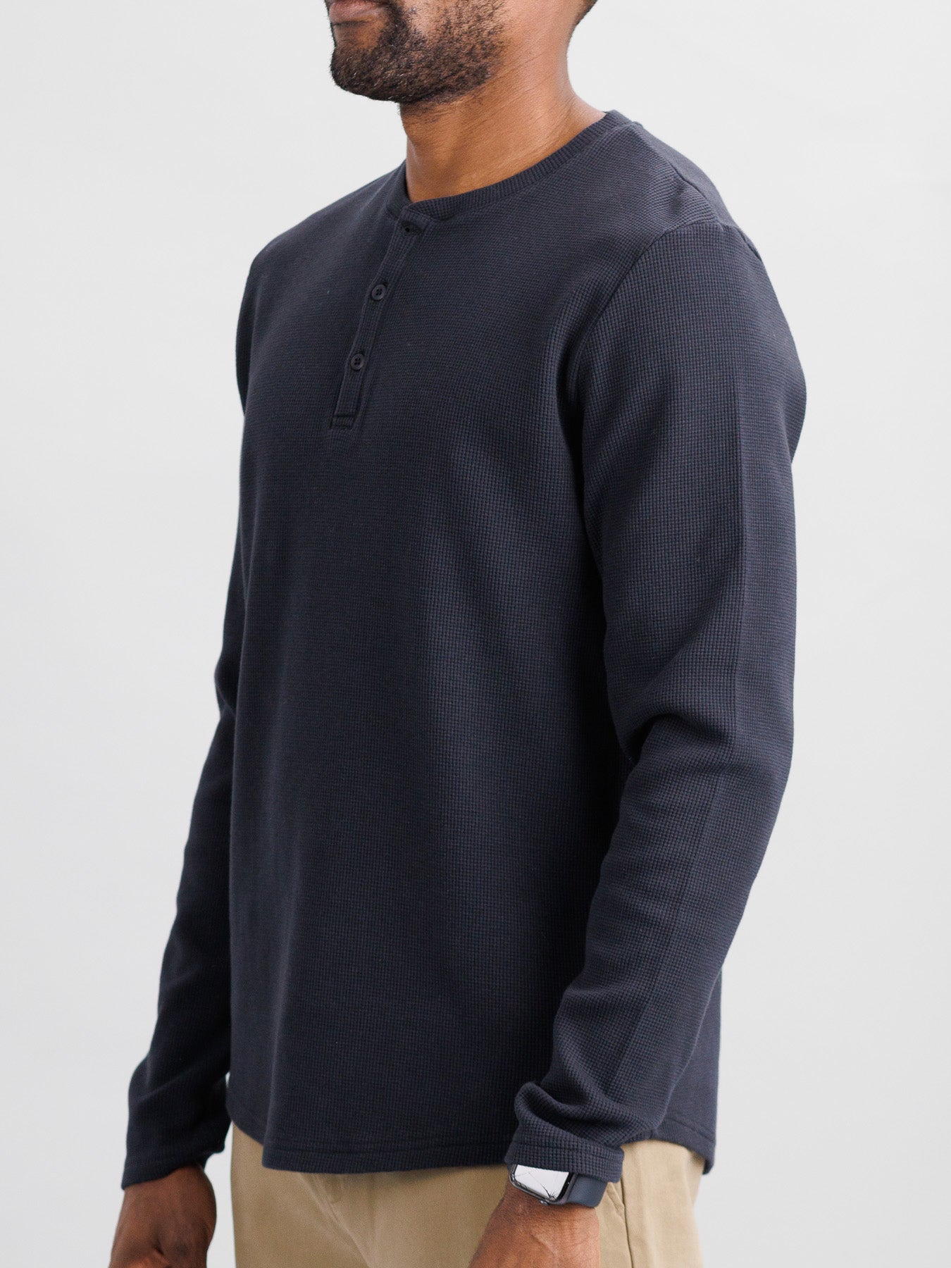 Someone is wearing an ID Menswear Freestyle Waffle Knit Henley with button details and beige pants. The regular fit enhances their look, and theyre sporting a watch on their left wrist. The background is plain and light-colored.
