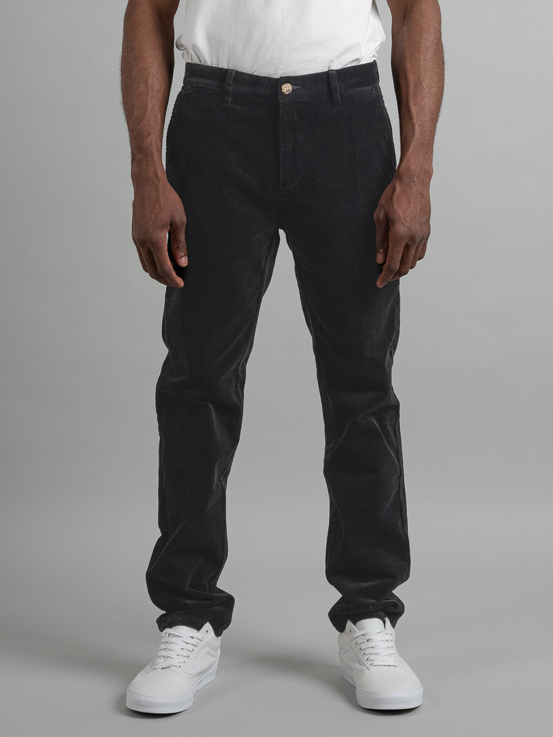 A person models Skillman Corduroy Pants by ID Menswear, wearing black straight-fit pants with a 32 inseam and a visible waist button. White sneakers complete the look against a neutral background, showing only the lower body in this smart-casual ensemble.