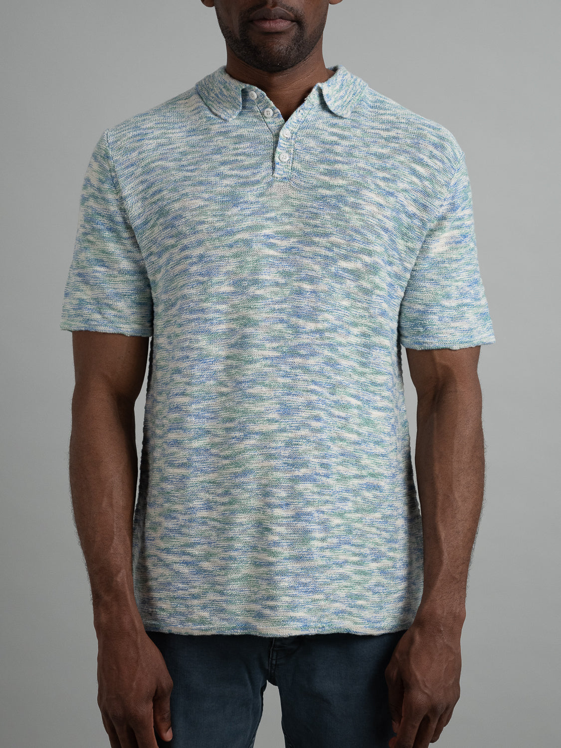 A man models the Miami Reverse Knit Cotton Polo by ID Menswear, showcasing its short sleeves and subtle blue-green pattern. The shirt features a collar, a short button placket, and offers a breathable fit against a plain light gray background.