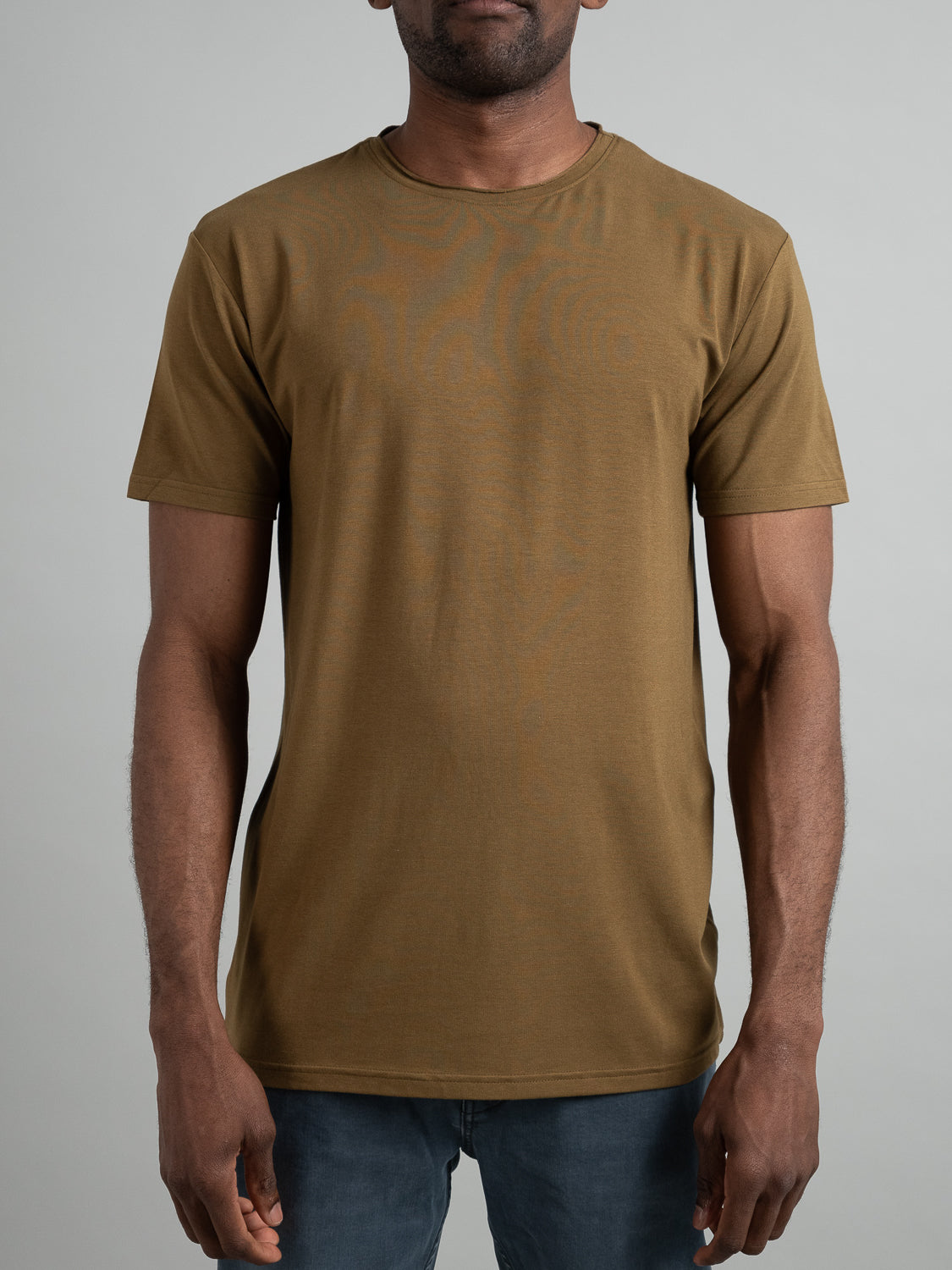 A man wearing ID Menswears Bello Bamboo Blend Rolled Neck Tee and jeans stands against a neutral background. This sustainable, short-sleeve shirt emphasizes eco-friendly style with its simple design. The image focuses on the upper body.