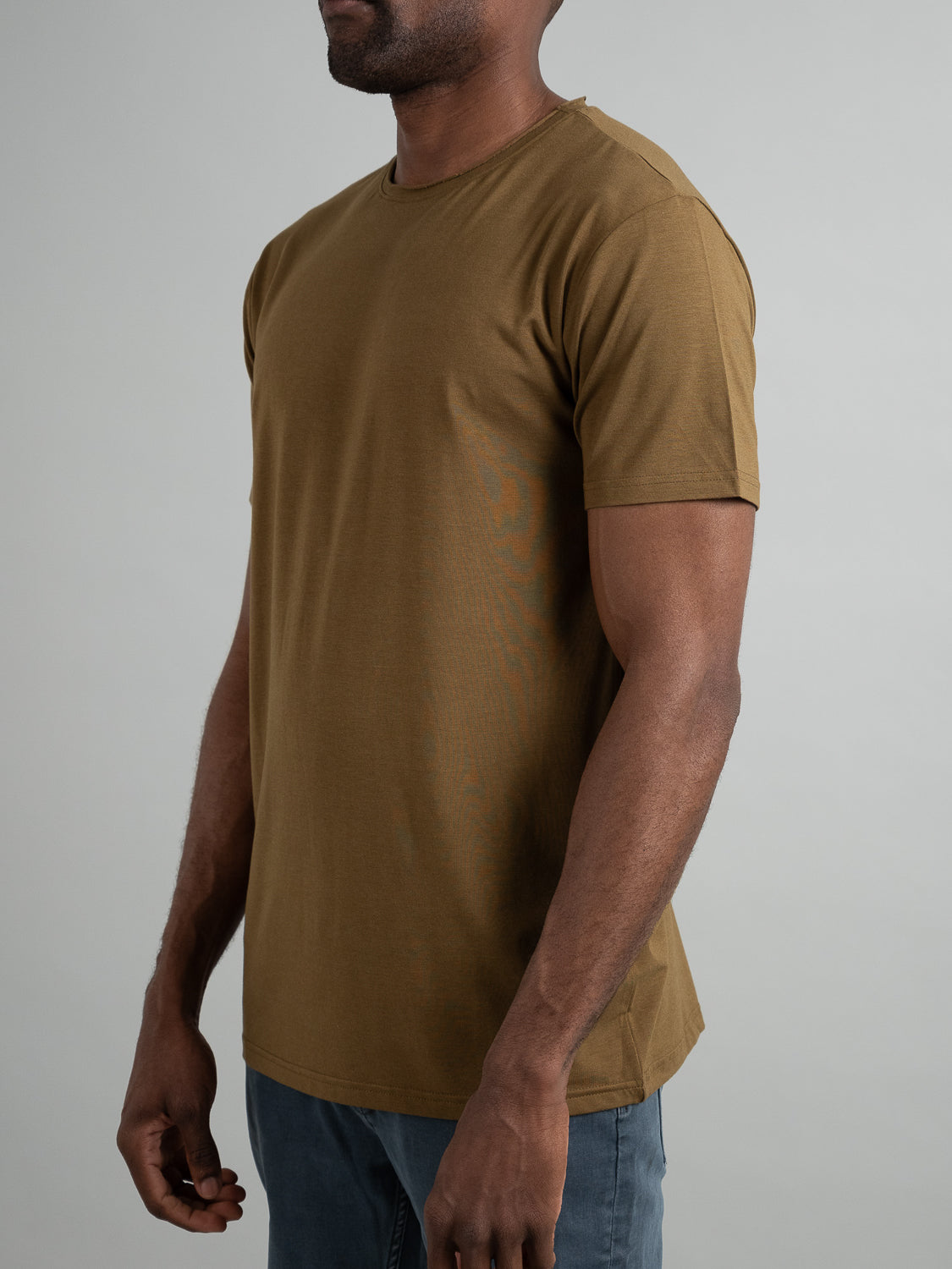 Someone in a Bello Bamboo Blend Rolled Neck Tee by ID Menswear and blue jeans stands against a neutral background. With their face turned away, they highlight the tees sustainable comfort and simplicity.