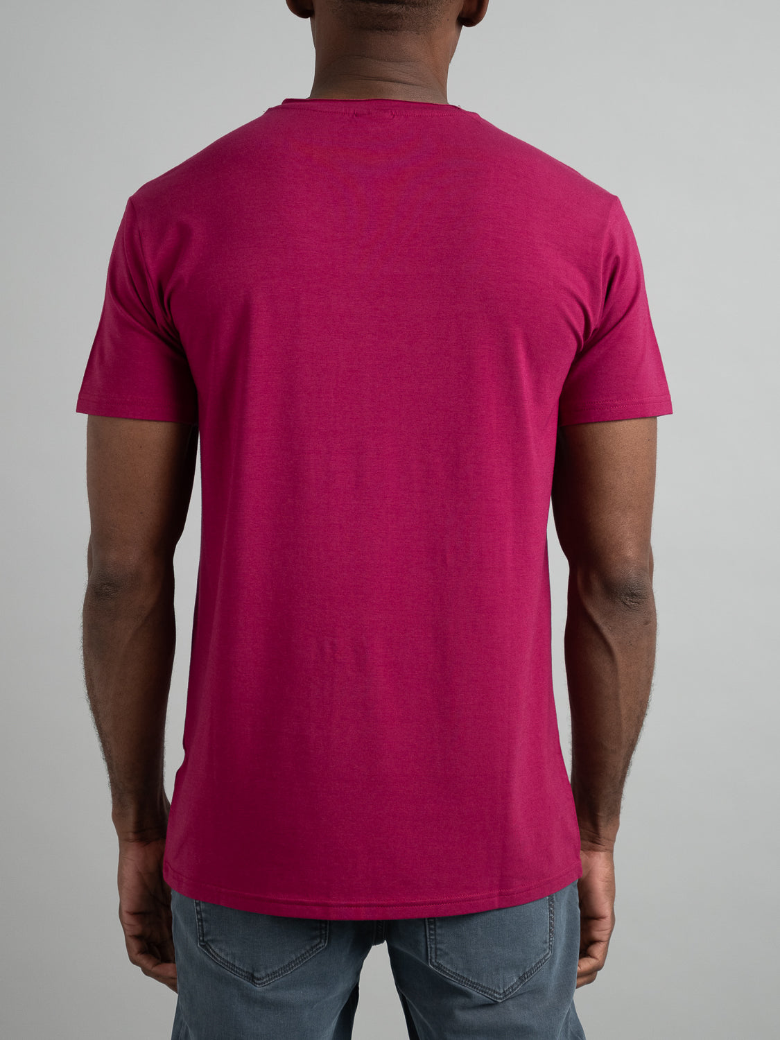 A man wearing a vibrant pink Bello Bamboo Blend Rolled Neck Tee by ID Menswear and gray pants stands with his back to the camera against a plain background.