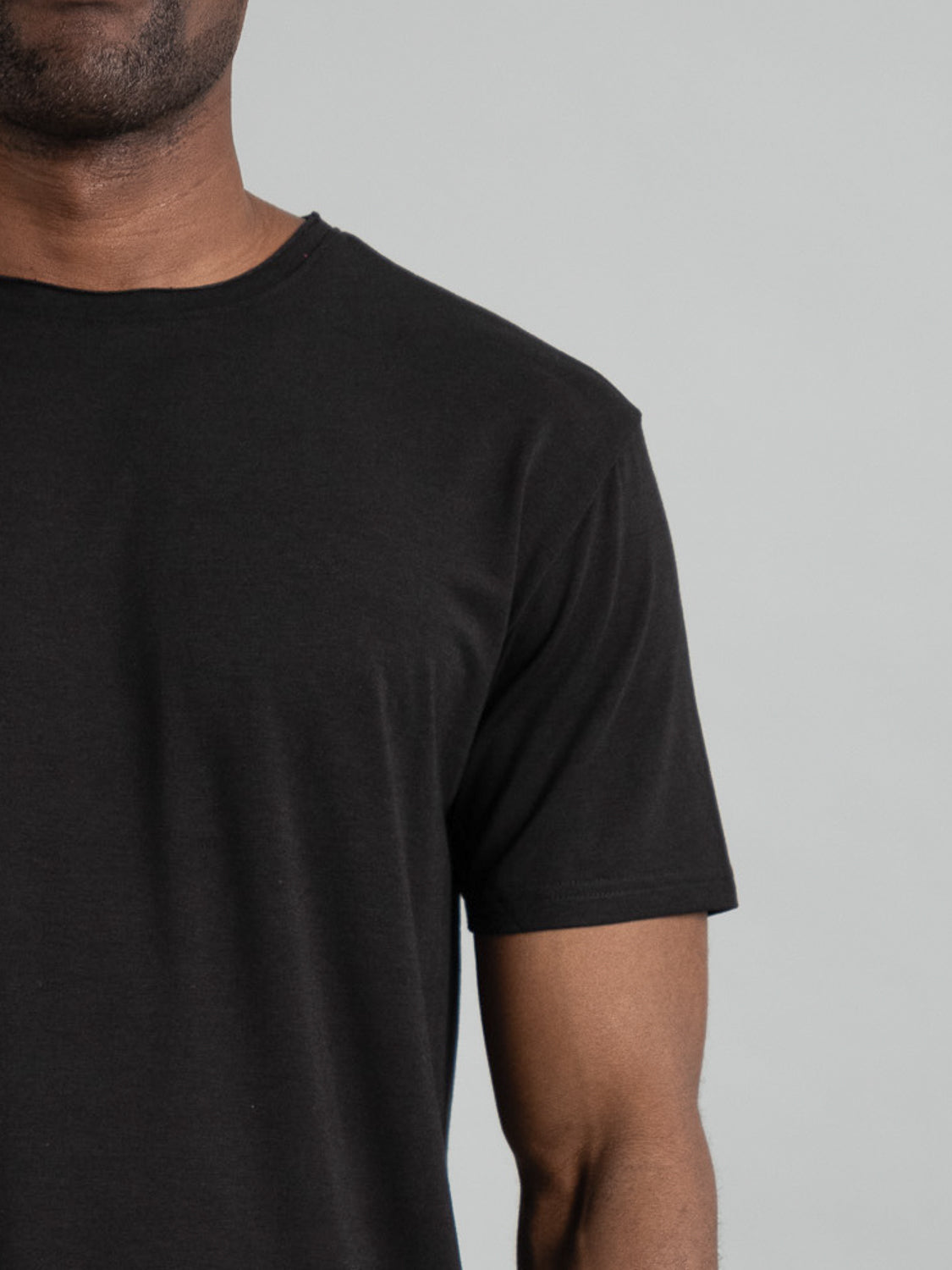 A person wearing ID Menswears Bello Bamboo Blend Rolled Neck Tee in plain black, visible from the neck to mid-arm against a light gray background.