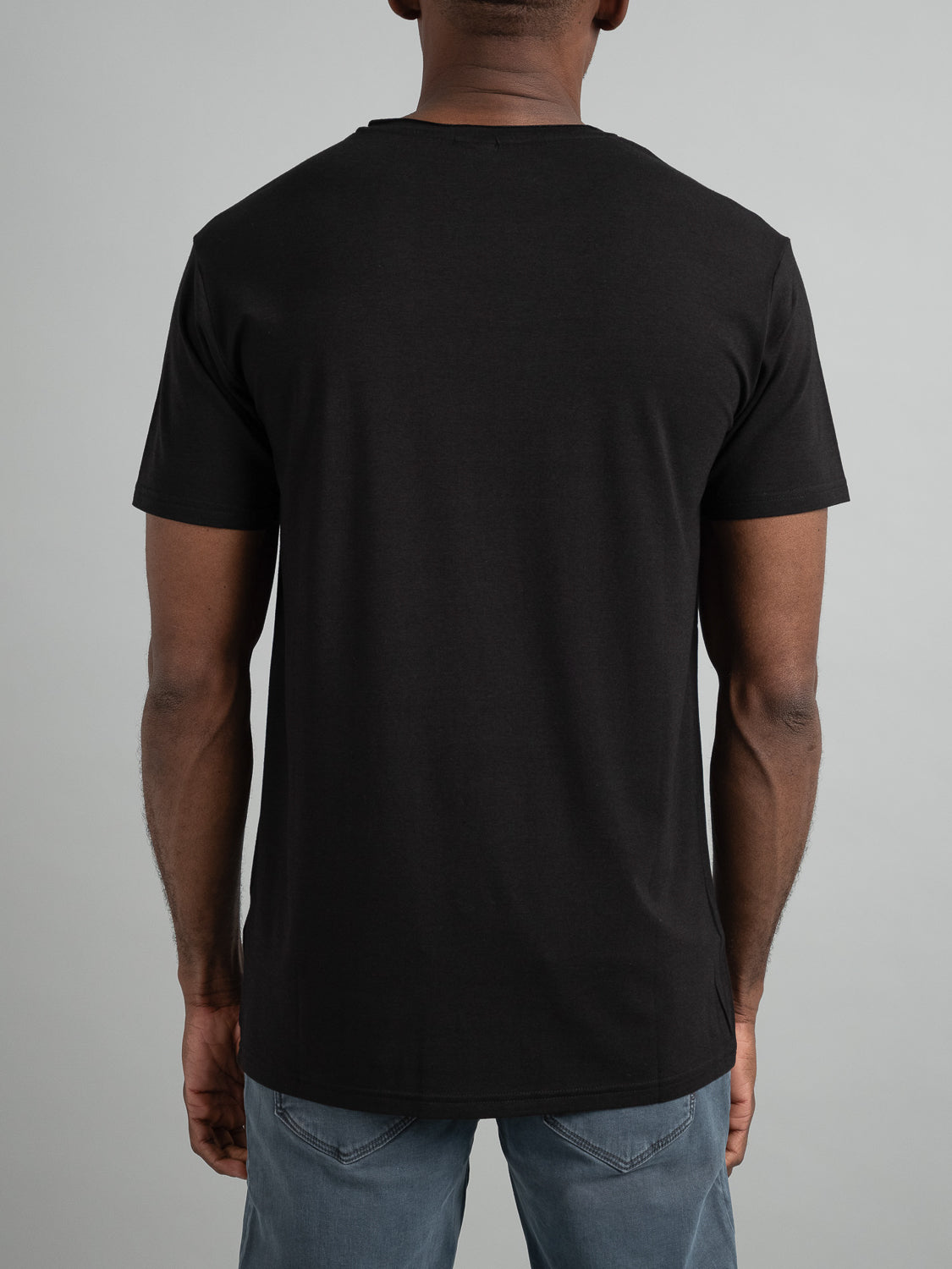 A person is wearing the Bello Bamboo Blend Rolled Neck Tee by ID Menswear in black and light blue jeans, photographed from behind against a light gray background.