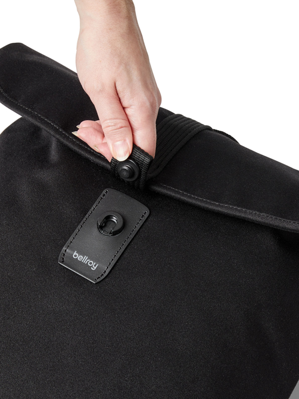 A hand closes a black Bellroy Oslo Backpack by fastening a snap button on the leather strap near the top.