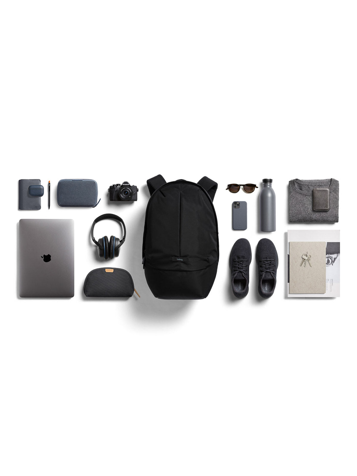 Travel essentials arranged on a white background, featuring the Bellroy Classic Backpack Plus - 24L (water-resistant, recycled fabric, dual compartments), headphones, sneakers, camera, sunglasses, water bottle, phone, tablet, pen, wallet & folded clothes.