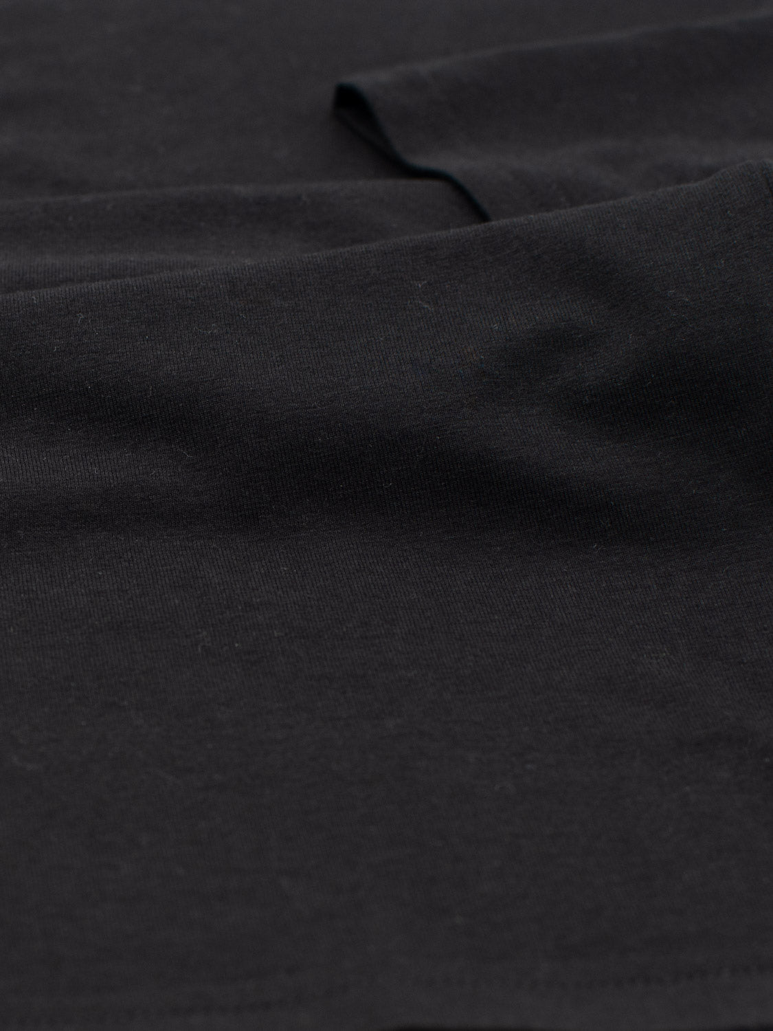 Close-up of Bello Bamboo Blend Rolled Neck Tee by ID Menswear, showcasing its black fabric texture and weave. The smooth, slightly reflective material evokes luxury with subtle folds creating gentle shadows.