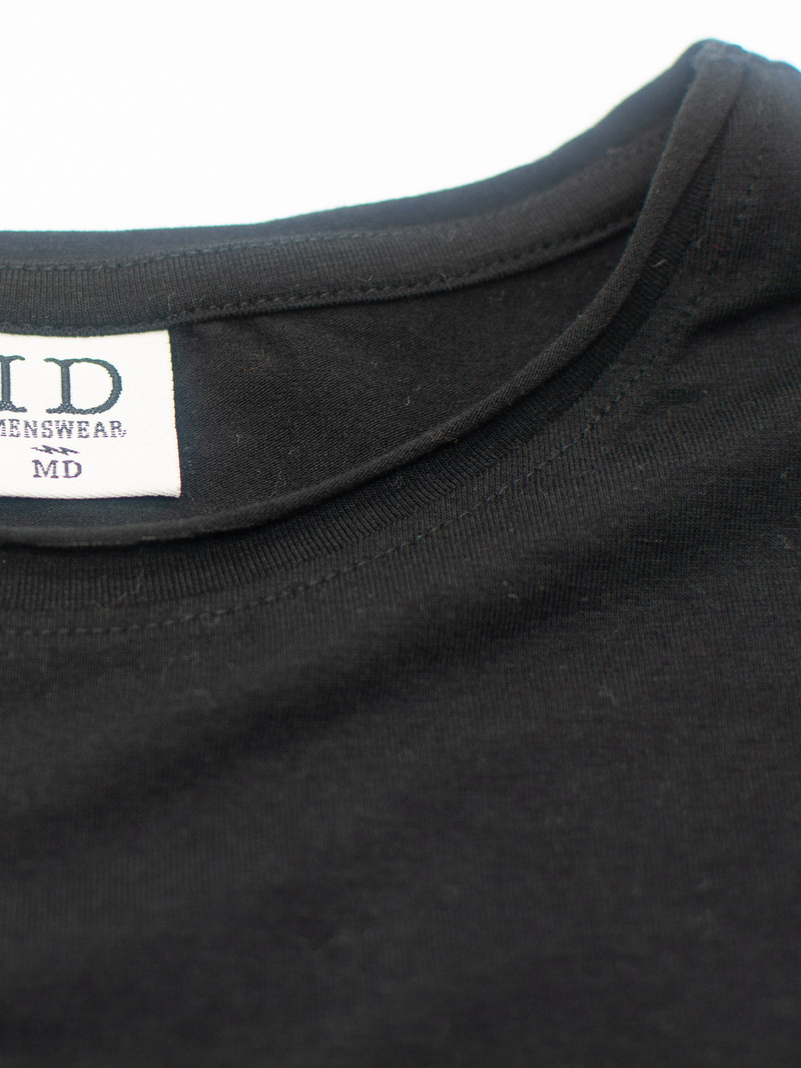 Close-up of a black rolled-neck T-shirt made from a bamboo blend, featuring an inside tag reading ID MENSWEAR in black on white. The visible stitching and fabric texture emphasize its commitment to sustainable clothing.