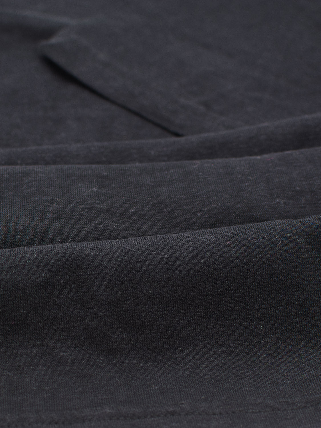 Close-up of the Dope Hemp Organic Cotton Tee by ID Menswear shows its dark grey, textured fabric with subtle folds and a weave pattern. The sustainable fabric looks soft, finely woven, and slightly shiny, highlighting its eco-friendly elegance.