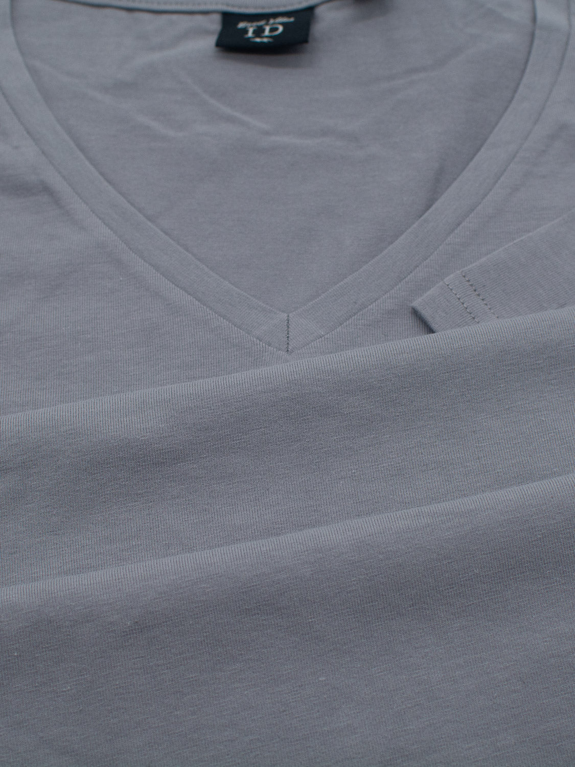 A sleek gray Form V Neck Tee from ID Menswear lies flat, slightly folded, with visible neckline stitches. Ideal for casual occasions, its form-fitting design is highlighted by a black back tag, showcasing simplicity against smooth fabric.