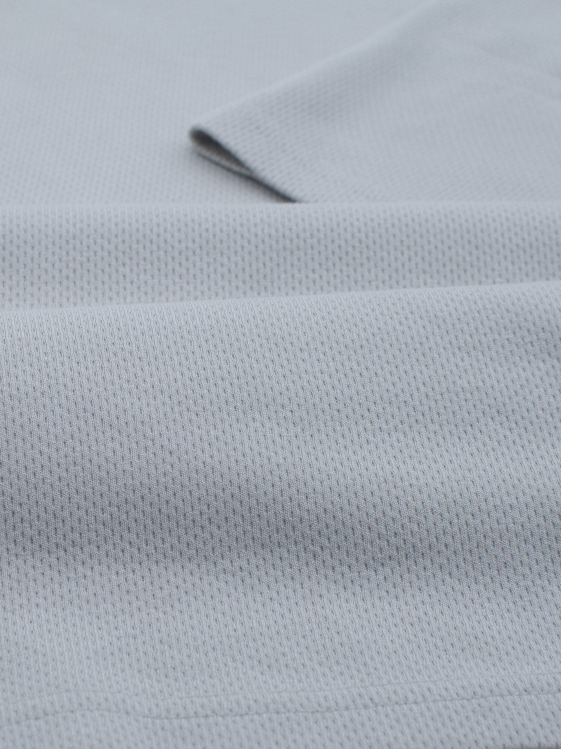 Close-up of Urban Honeycomb Mesh Tee fabric by ID Menswear, featuring a light blue textured bamboo-organic cotton blend with a breathable grid pattern. The gentle folds create soft shadows and highlights, accentuating the delicate knitwork.