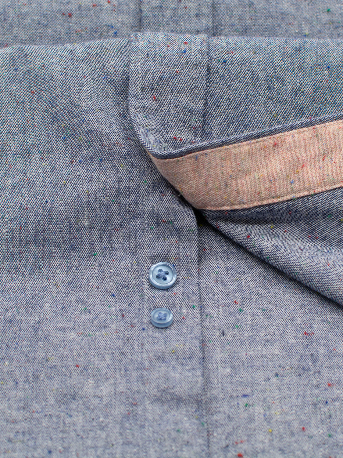 Close-up of a gray fabric with colorful specks and a partially open button placket on the ID Menswear Allswell Speckled Button Down Shirt. Two gray buttons are fastened, revealing a beige inner lining. Made from premium cotton-linen blend, it boasts a soft texture and detailed design.