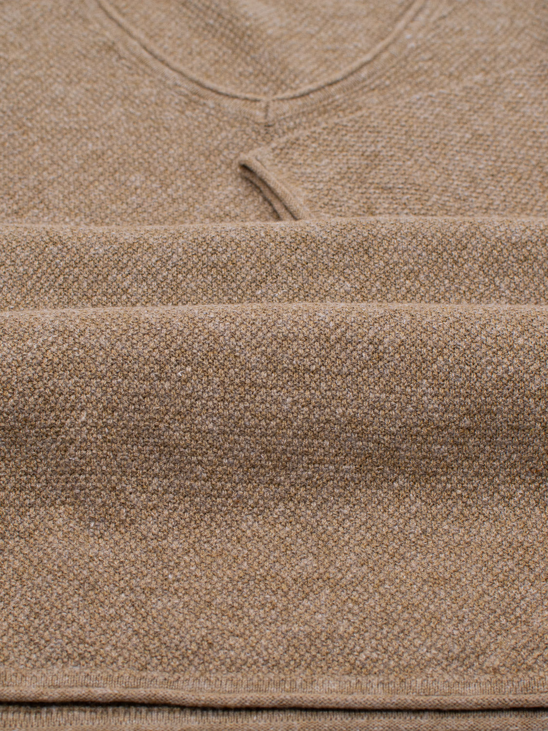 A close-up of the Amalfi Deep V Knitted Top by ID Menswear shows its textured knit pattern in a beige linen-cotton blend, featuring visible seams and subtle v-stitch near the deep V-neck.
