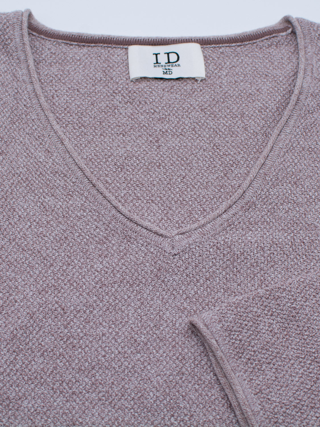 A close-up of a light purple Amalfi Deep V Knitted Top from ID Menswear shows the visible tag reading ID and MD. The sweater features a soft, textured fabric with a deep V-neck and a partially visible folded sleeve at the bottom right.