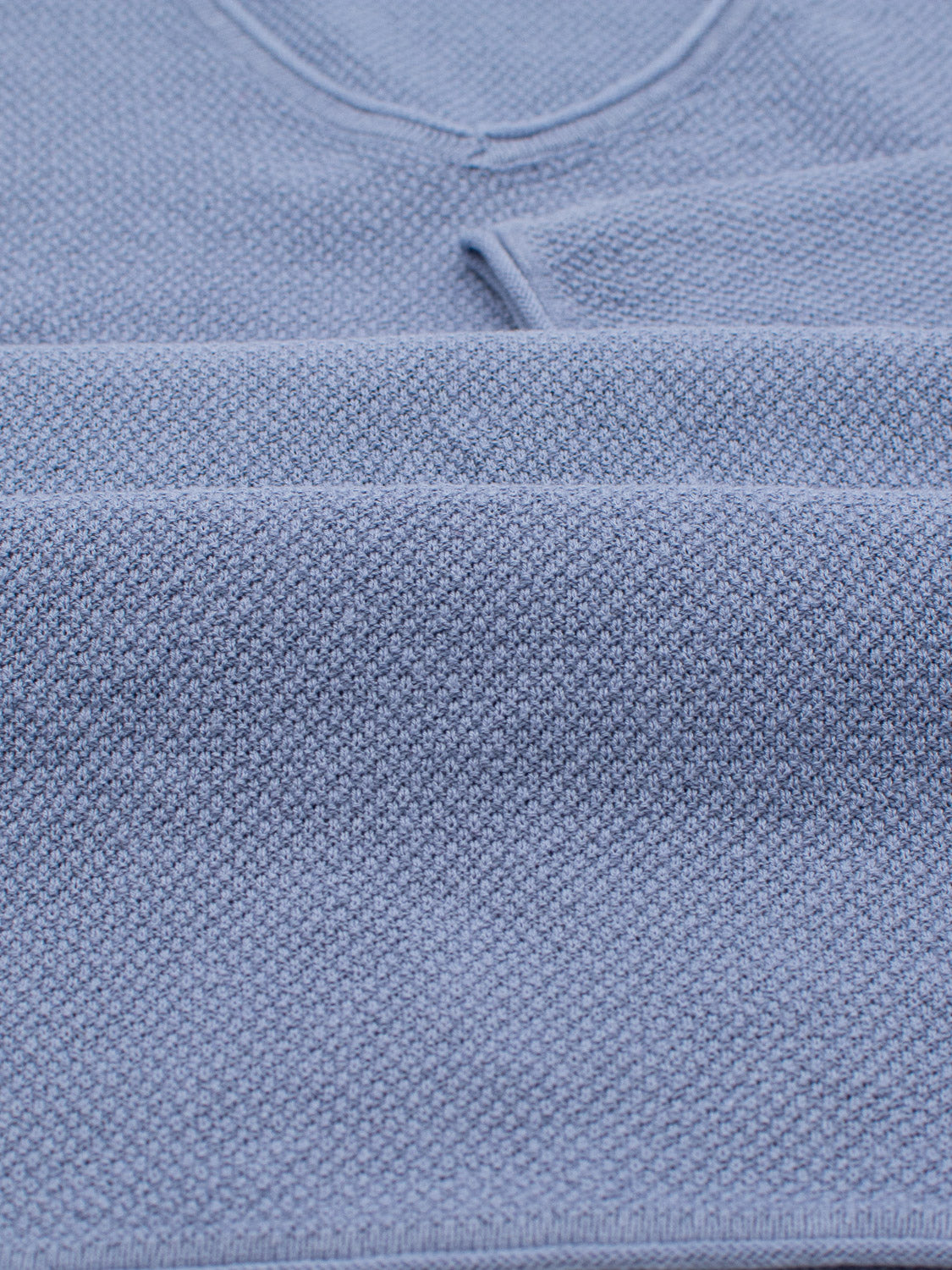 Close-up of folded blue textured fabric, likely an Amalfi Deep V Knitted Top by ID Menswear, showcasing its detailed knit pattern and soft appearance, crafted from a luxurious linen and cotton blend.