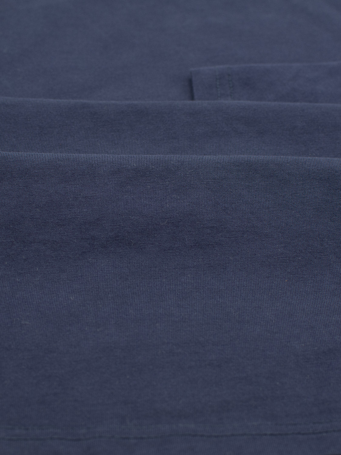 A close-up of folded dark blue fabric highlights its texture and gentle folds, ideal for crafting a comfortable ID Menswear Sublime Long Sleeve Tee from organic cotton.