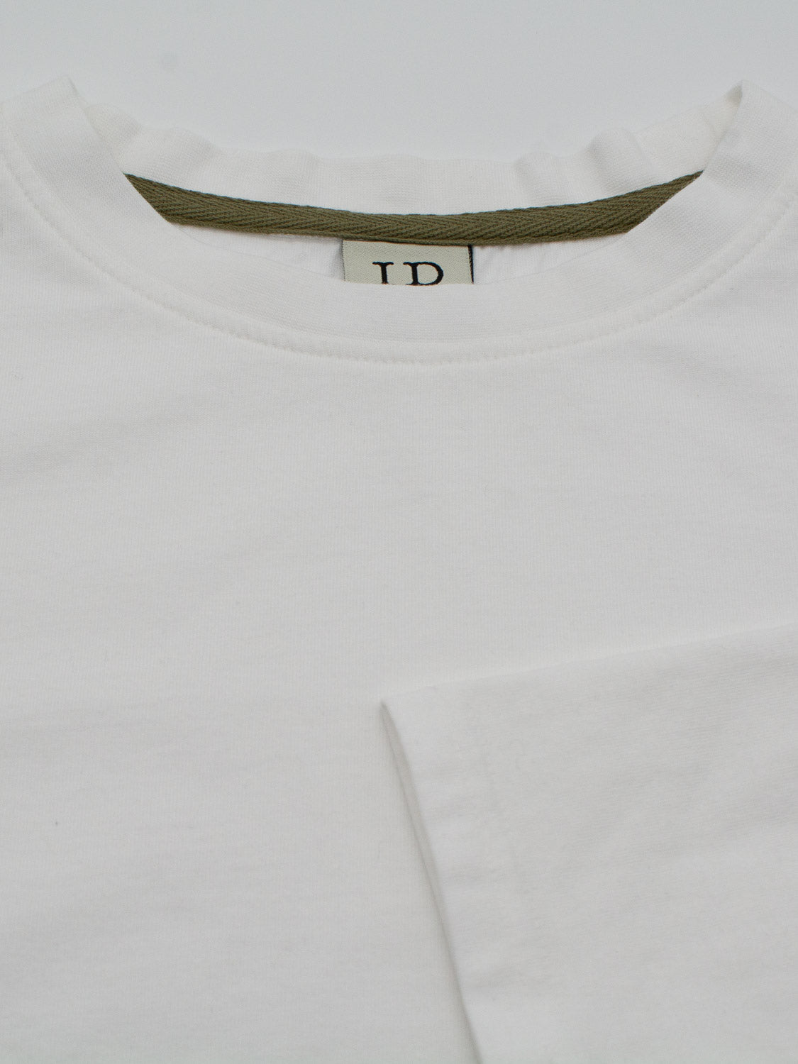 Close-up of a white crew-neck Sublime Long Sleeve Tee by ID Menswear, featuring an olive green inside collar. Made from organic cotton, the fabric looks soft and smooth, ideal for casual wear. The neck label displays the letters ID.