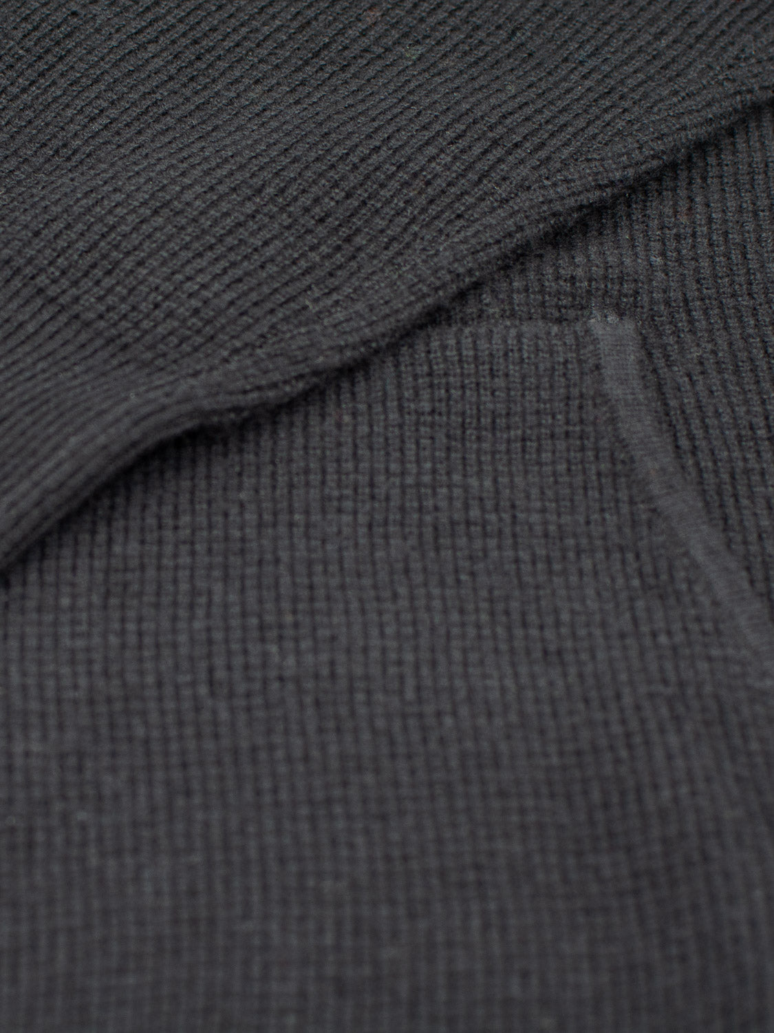 Close-up of the Bergen Waffle Knit Merino Hoody from ID Menswear, featuring a dark gray, ribbed texture. Overlapping sections highlight its soft, cozy appearance, reminiscent of a warm hoody.