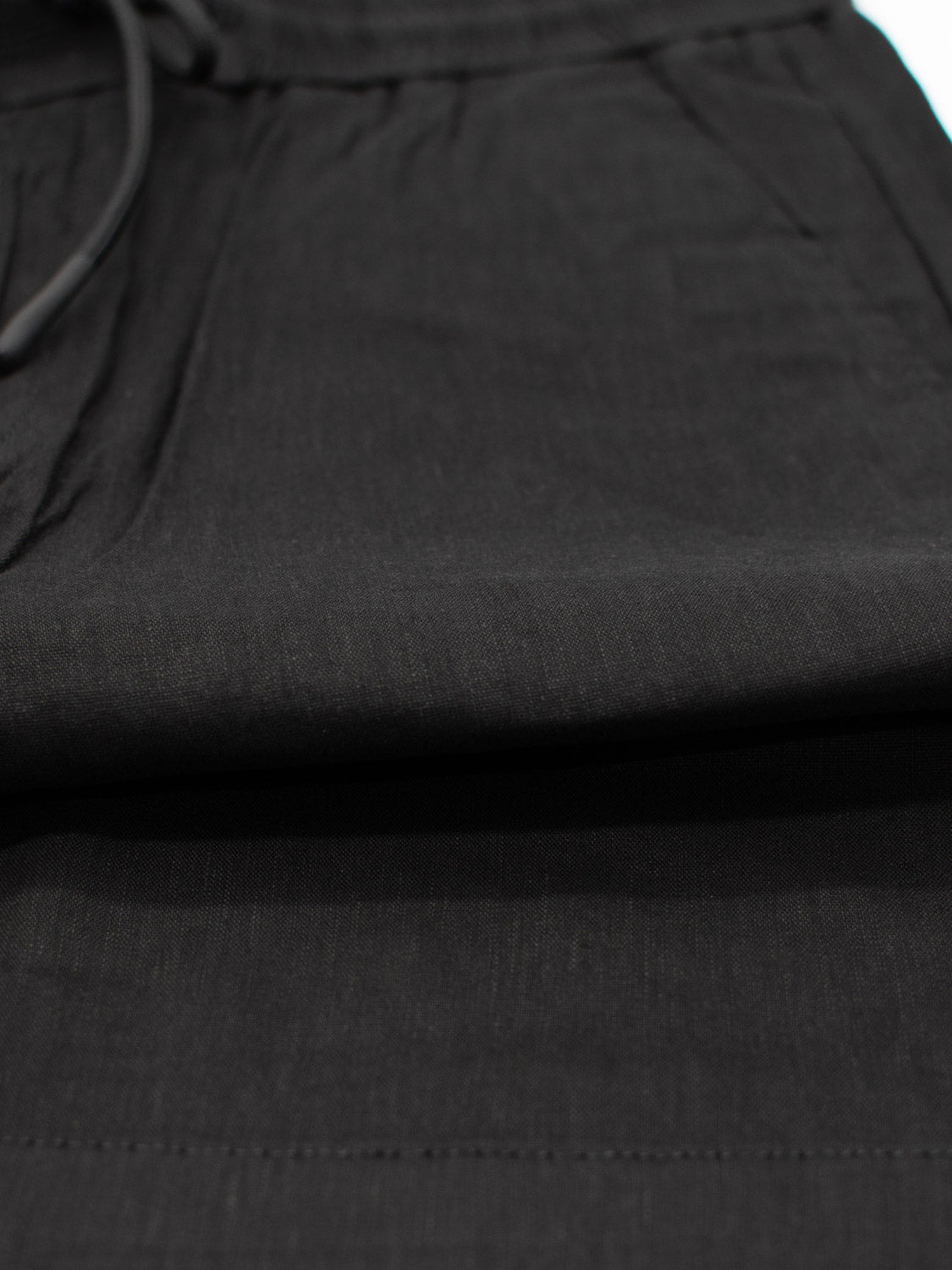 Close-up of Driggs Linen Blend Short by ID Menswear, showcasing the waistband and drawstring. The black fabric is smooth with subtle horizontal lines, ideal for warm weather. The image emphasizes the versatile upper section of these shorts.