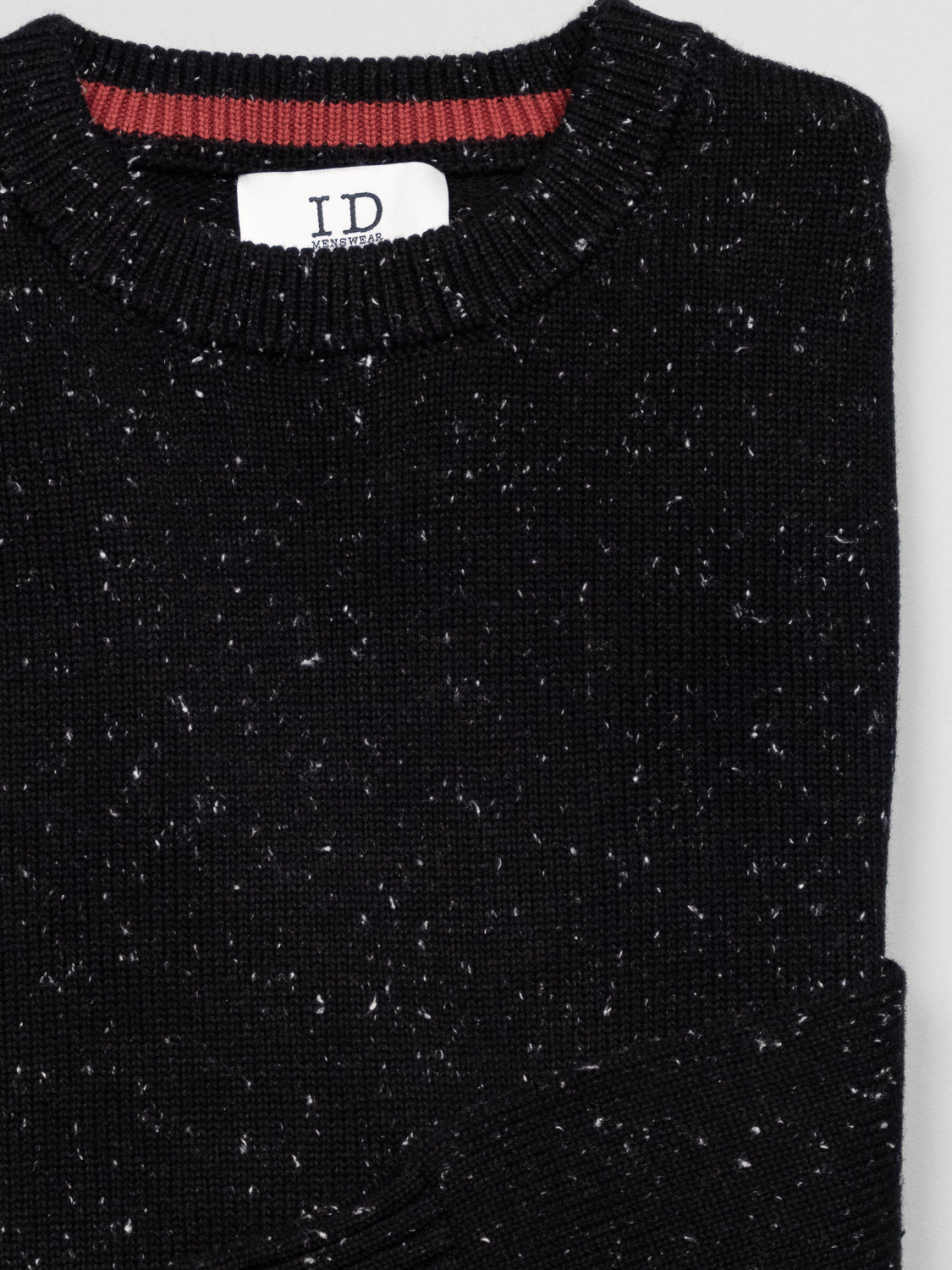 The Malmo Speckled Cotton Sweater by ID Menswear is folded on a light gray surface. It features a plain knit design with white specks on black and a ribbed crew neckline. A white ID label is visible at the collar.