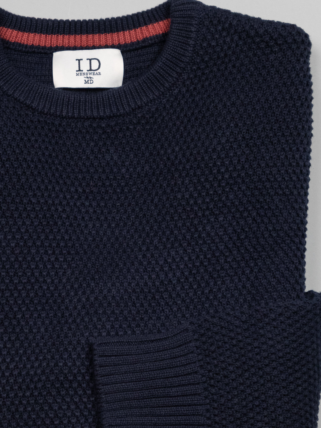 Close-up of a cozy, stylish dark blue Quebec Chunky Sweater featuring a textured Moss knit pattern. The visible label reads ID Menswear. The image highlights the sweaters intricate weave and sleeve cuff against a light grey background.
