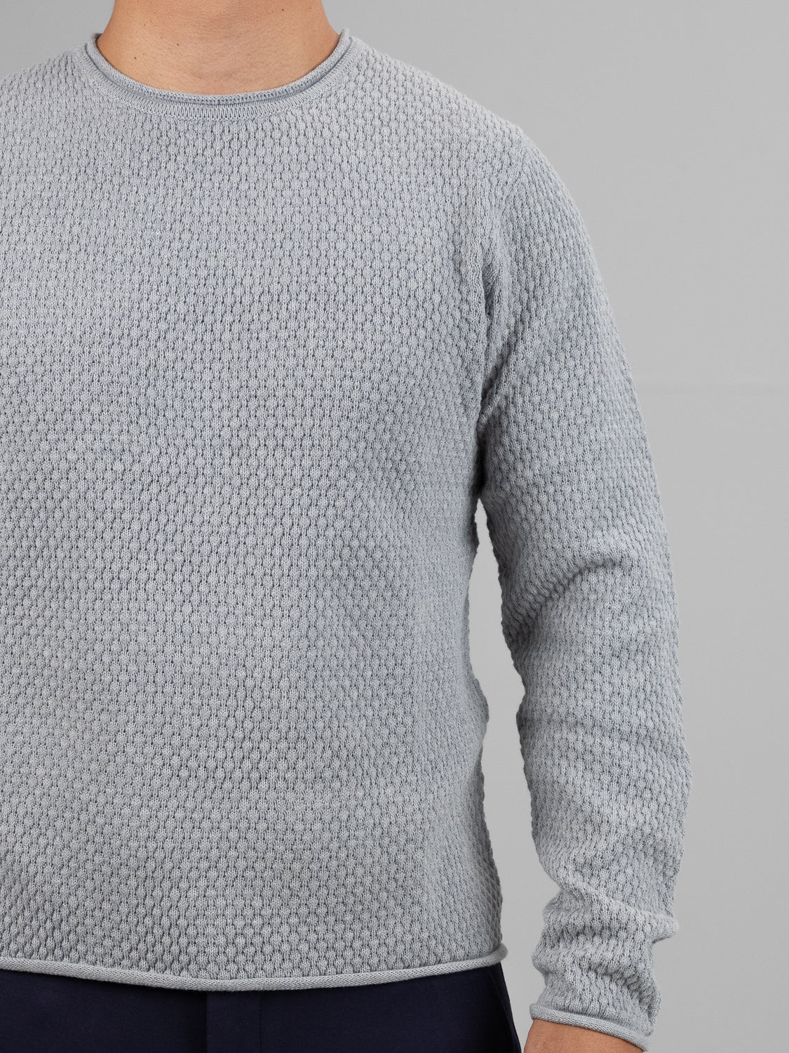 A person wearing a light gray ID Menswears Westside Rolled Neck Sweater with a waffle-knit pattern stands against a plain gray backdrop. Their face is hidden, and their left arm is slightly folded, capturing the essence of casual knitwear.