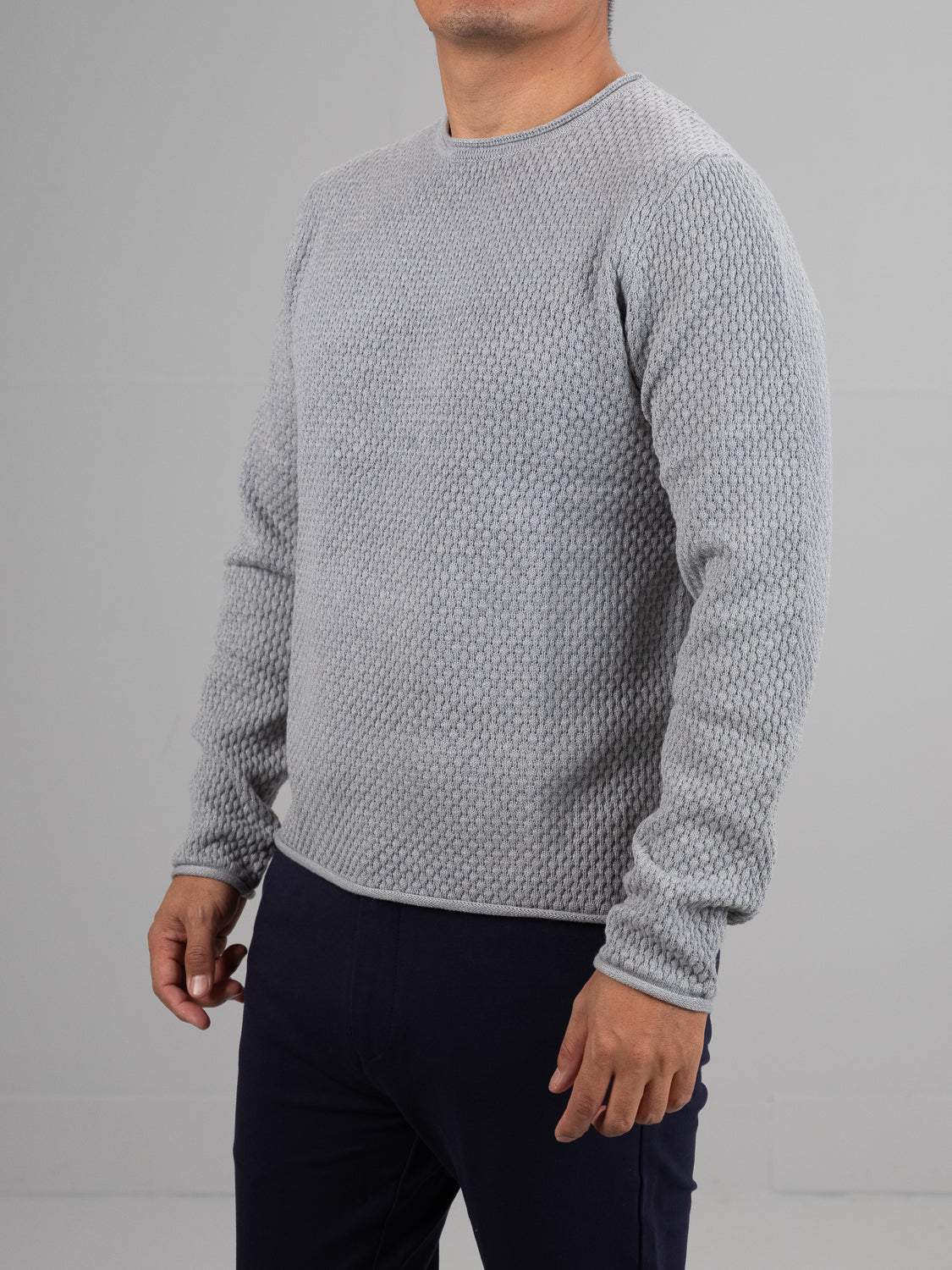 A person wears a gray ID Menswear Westside Rolled Neck Sweater with textured long sleeves and dark pants, standing against a plain background. Their face is not visible.