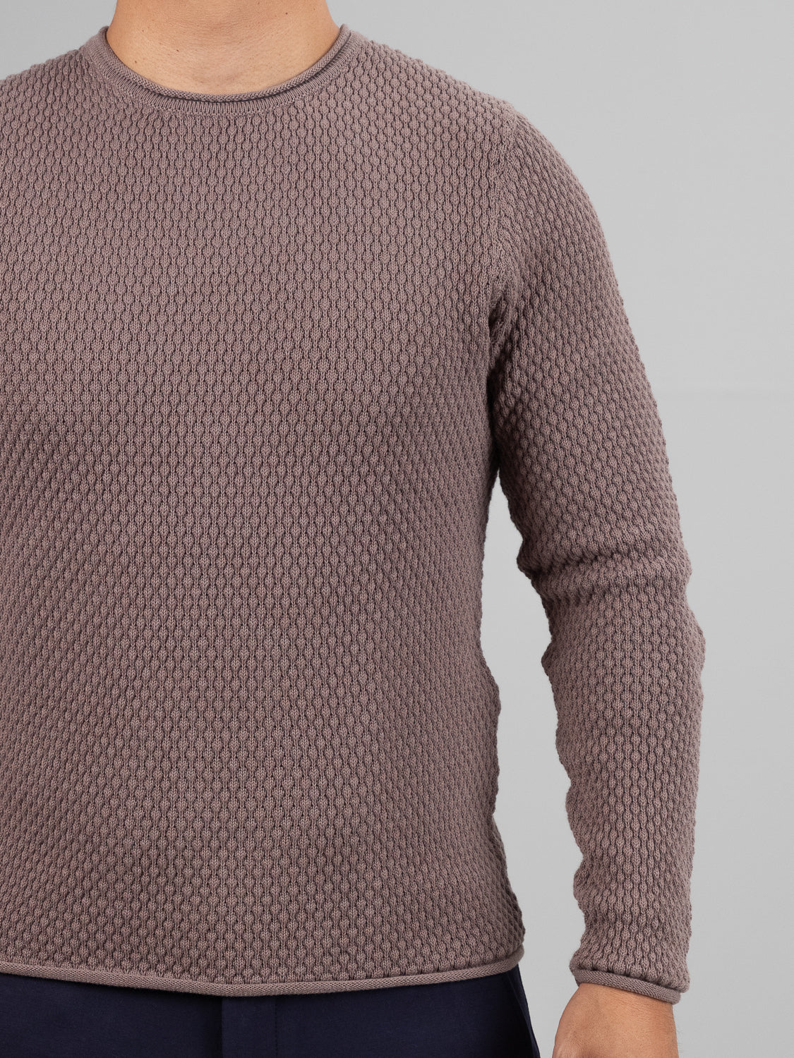 A person in a textured taupe Westside Rolled Neck Sweater and dark pants by ID Menswear stands against a gray background. The casual knitwear features a raised waffle-like pattern. The head is not shown in the image.