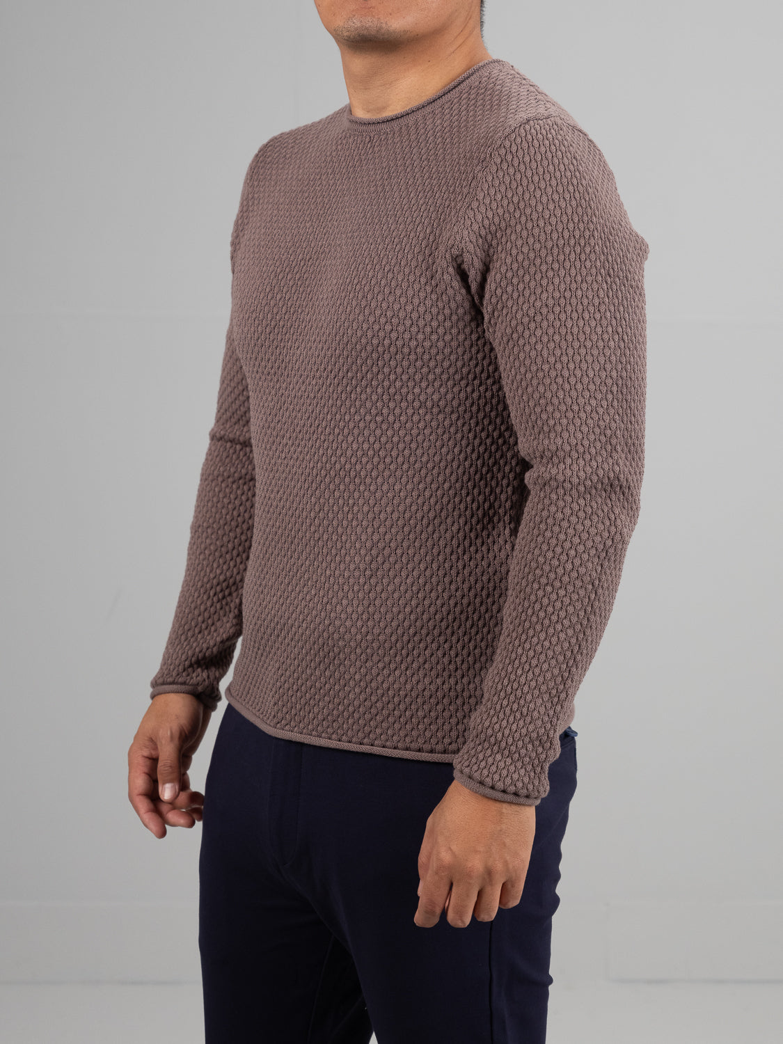 Someone wearing the Westside Rolled Neck Sweater from ID Menswear, a textured, long-sleeve brown design with an intricate waffle-knit pattern, paired with dark pants stands against a plain backdrop with their head out of frame.
