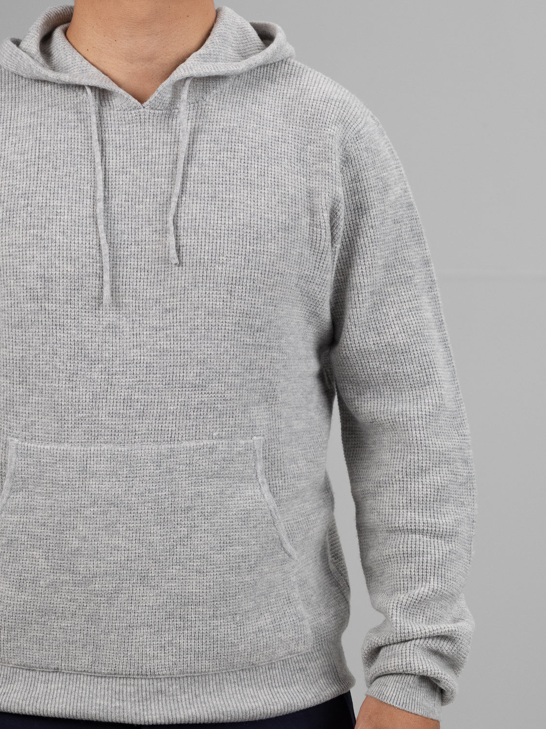 Someone is wearing the Bergen Waffle Knit Merino Hoody by ID Menswear in light gray. The hoodie features long sleeves, a front pocket, and drawstrings. Only their upper body is visible against a plain background.