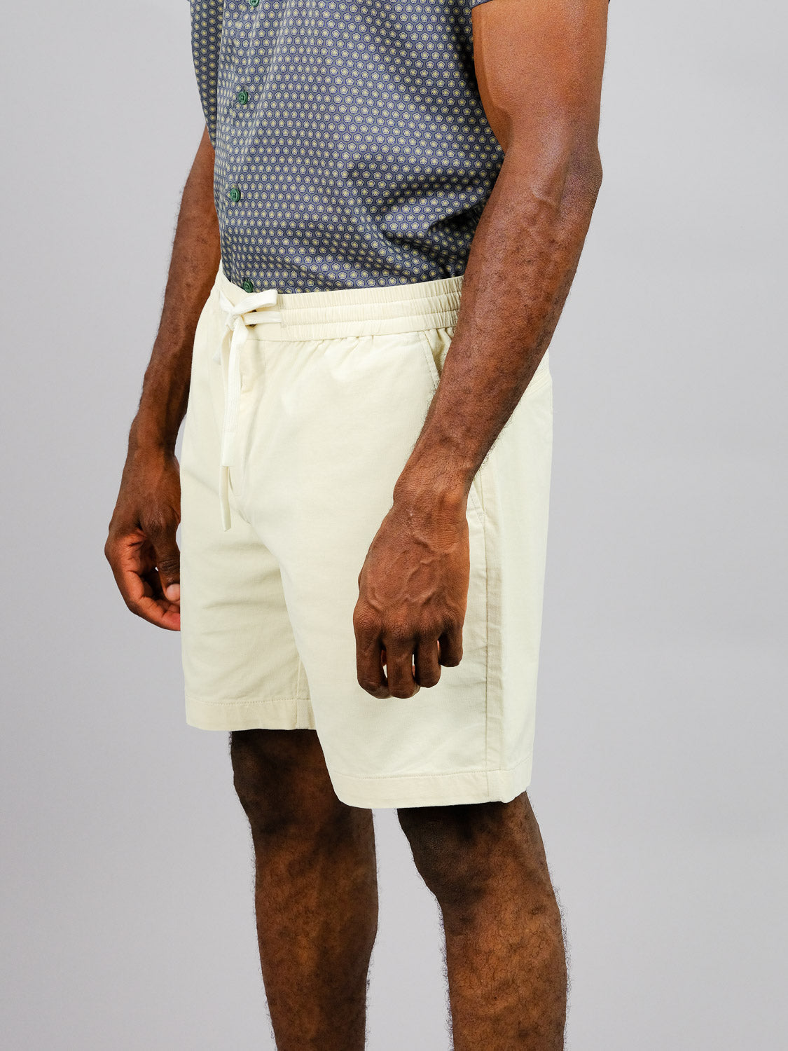 A person in a gray patterned shirt and ID Menswears Odyssey Corduroy Stretch Short with an elastic waistband stands against a plain backdrop, hands relaxed at their sides.