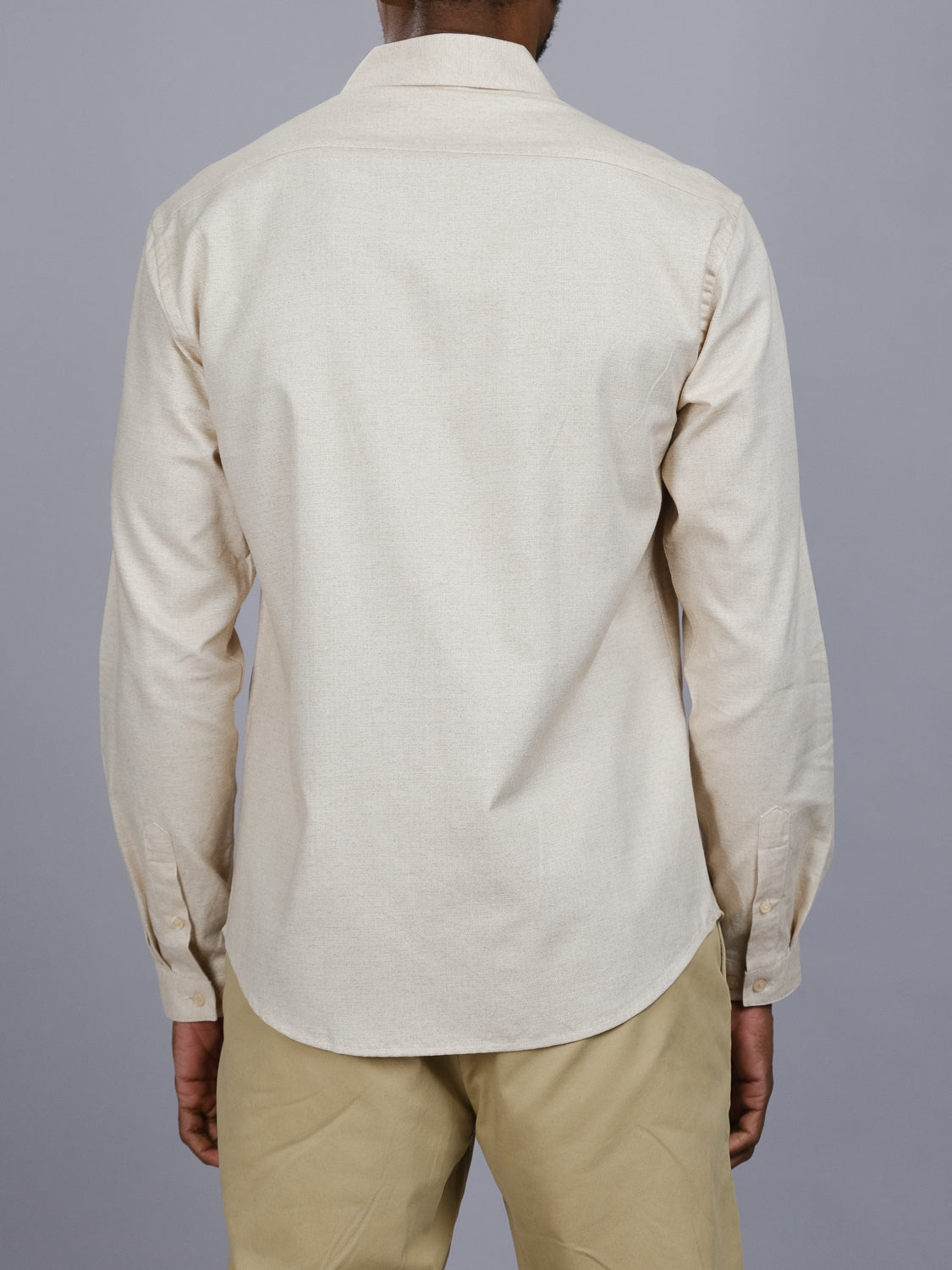A person is shown from the back against a gray background, wearing a beige Maya Fine Herringbone Shirt by ID Menswear and tan pants. The 100% cotton shirt is untucked, and their hands rest relaxed at their sides.