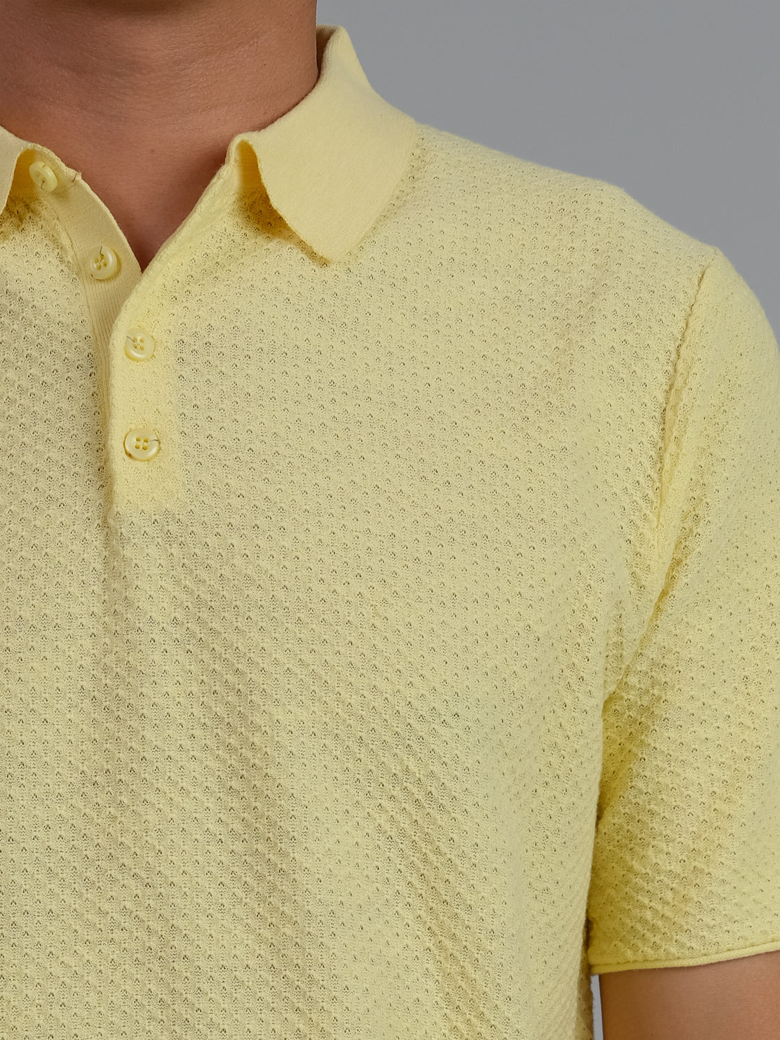 A person is wearing the Phoenix Super Fine Cotton Knit Polo, a yellow textured short-sleeve shirt with buttons from ID Menswear. This stylish, versatile look suits casual wear, showcased against a plain gray background focusing on the upper torso.