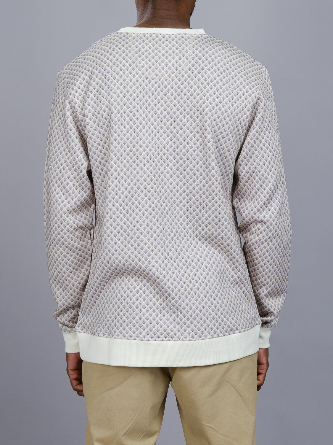 A person wearing the Carp Geometric Printed Sweatshirt by ID Menswear, made from bamboo and organic cotton fleece, stands with their back to the camera. The sweatshirt has a modern artistic vibe with its light-colored diamond pattern and beige pants against a plain gray background.