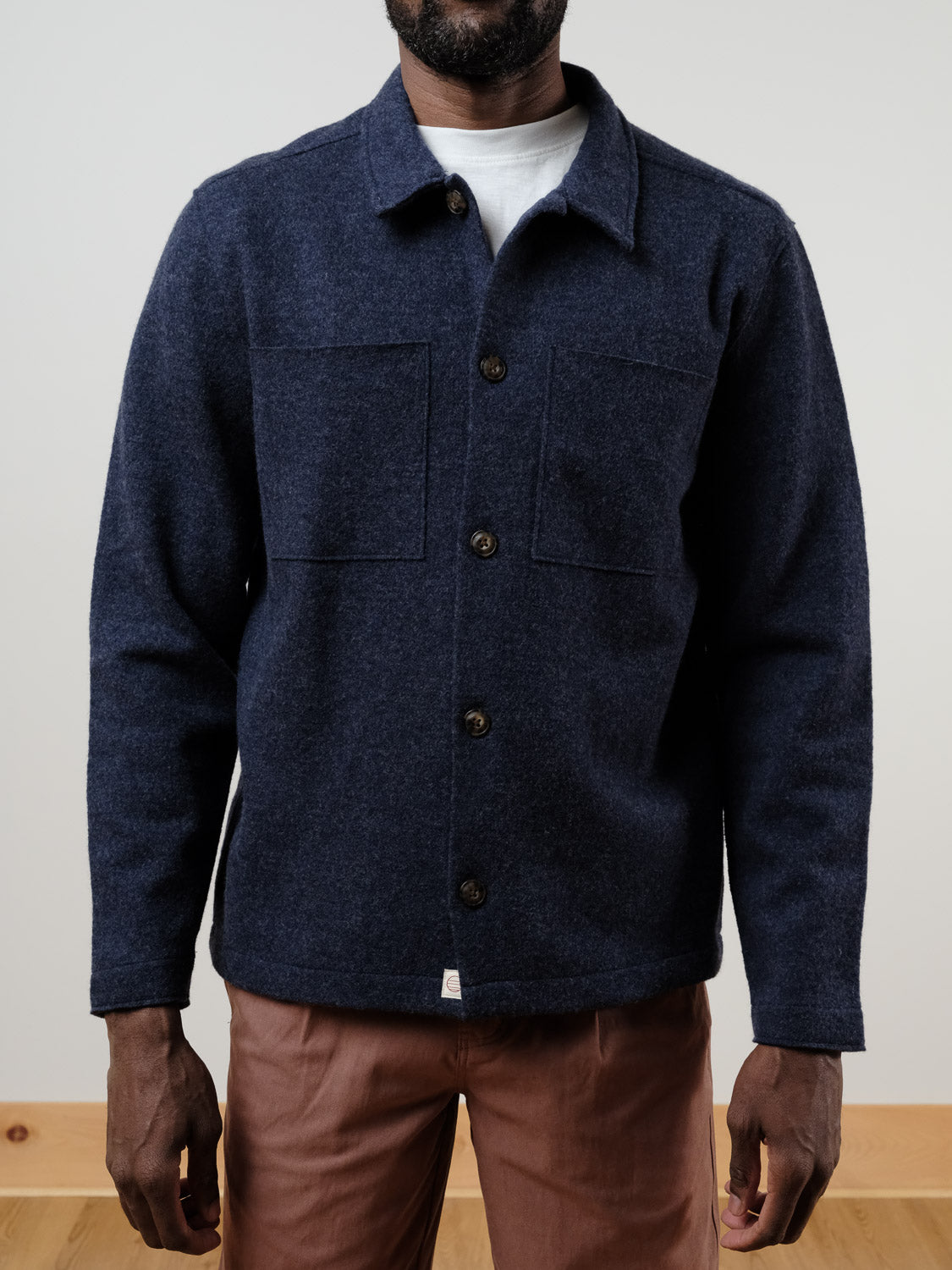 A person models the Marine Layer Mendocino Wool Overshirt in navy blue, layered over a white shirt and paired with light brown pants, standing against a plain background with hands relaxed at their sides.