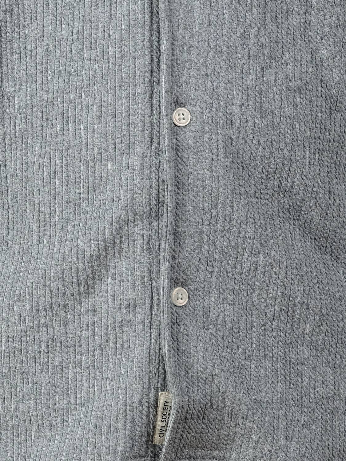 Close-up of a gray, ribbed knit Viggo Knit Resort Shirt by Civil Society featuring three visible buttons and a small fabric tag near the bottom edge.