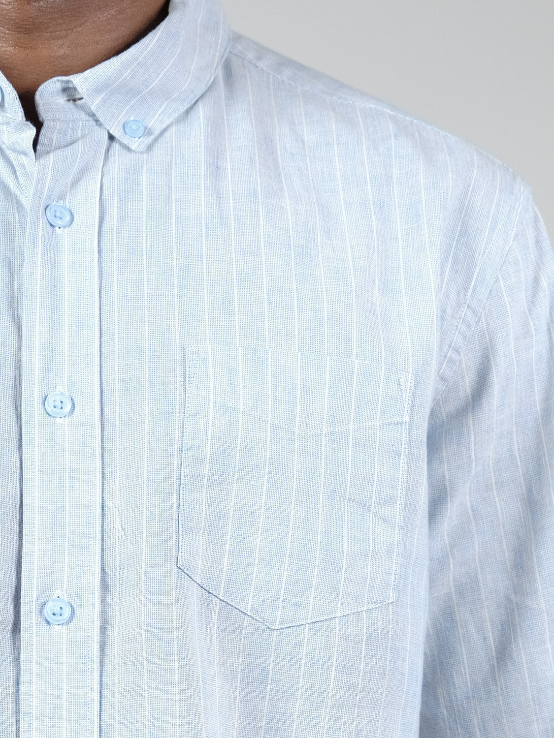 Close-up of a person wearing the Dubai Long Sleeve Shirt by ID Menswear, featuring light blue vertical pinstripes, a chest pocket, and visible collar and buttons against a plain neutral background.