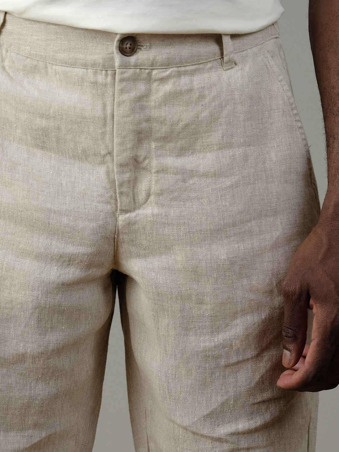 Close-up of a person wearing Casual Friday’s Pandrup Linen Pants in light beige with a button and zipper closure, paired with a white shirt. The person’s right hand is visible by their side.
