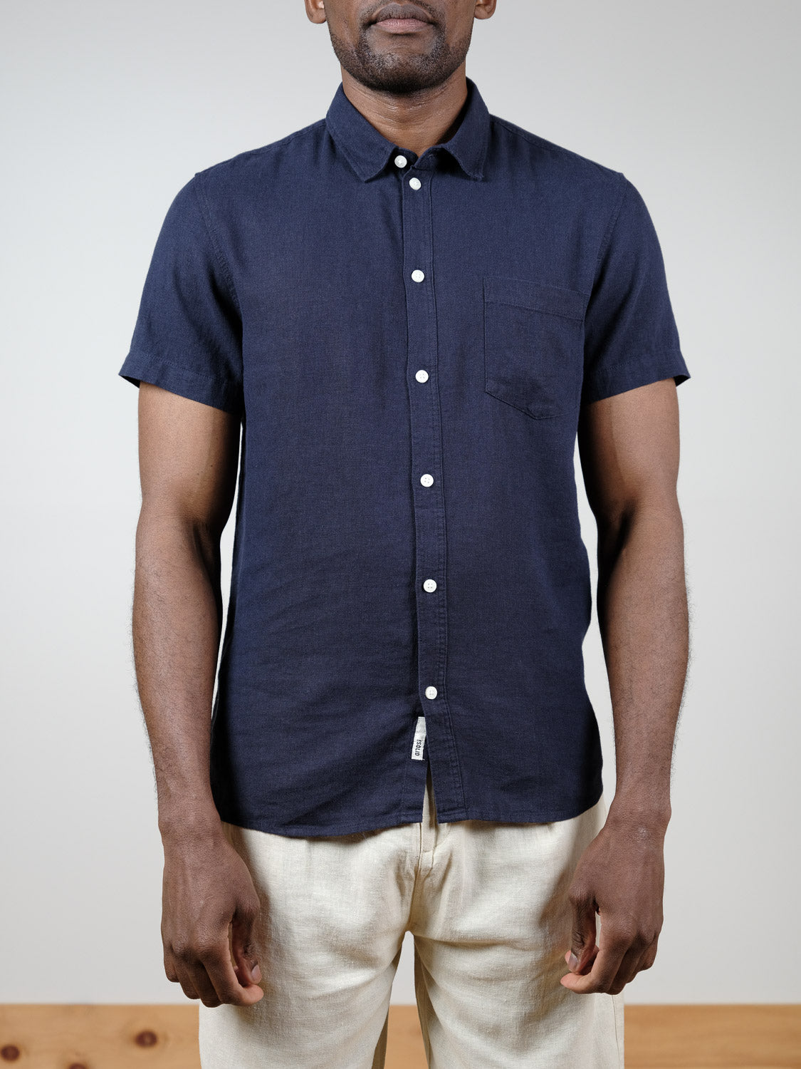 A person models the !Solid Allan Short Sleeve Shirt, featuring a chest pocket, paired with light pants against a plain backdrop. The breathable linen fabric ensures comfort. The person's face isn't visible.