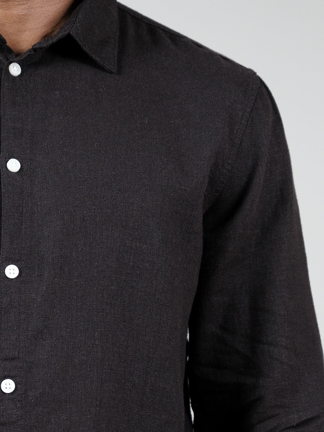Close-up of a person wearing the !Solid Enea Allan Long Sleeve Shirt in black with white buttons, showing chest, shoulder, and arm against a plain light gray background.