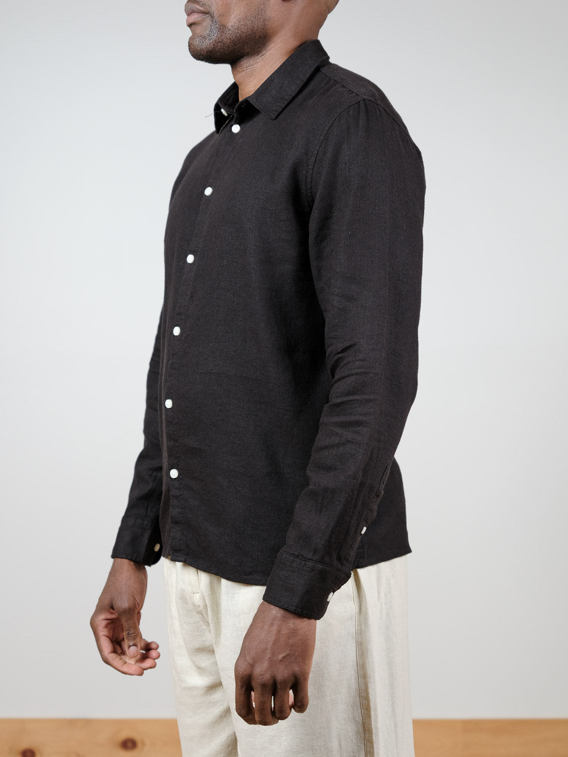 A man stands in profile against a plain light background, wearing the !Solid Enea Allan Long Sleeve Shirt in black with light beige pants.