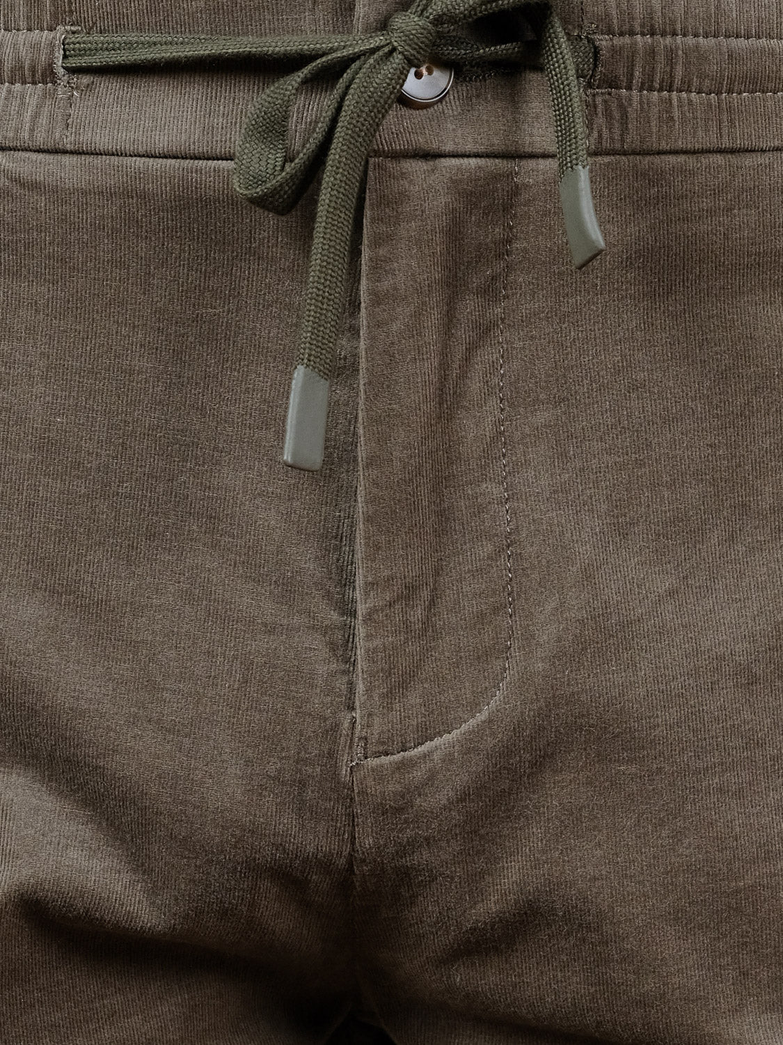 Close-up of the Odyssey Corduroy Stretch Short from ID Menswear in olive green, featuring an elastic waistband, button closure, drawstring with plastic tips, and a visible right pocket seam for a comfortable casual style.
