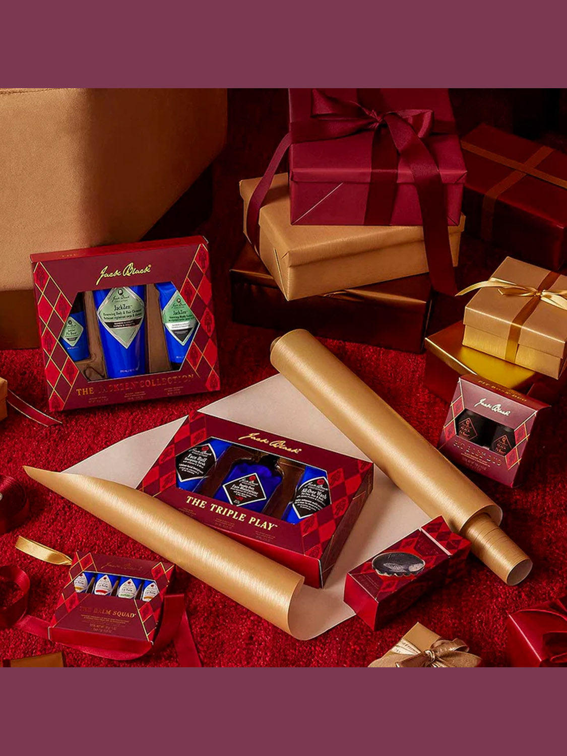 The JackZen™ Collection by Jack Black, in festive red and gold packaging, is displayed with body lotion, gold wrapping paper rolls, and ribbon-tied gifts on a red surface for a holiday-inspired showcase.