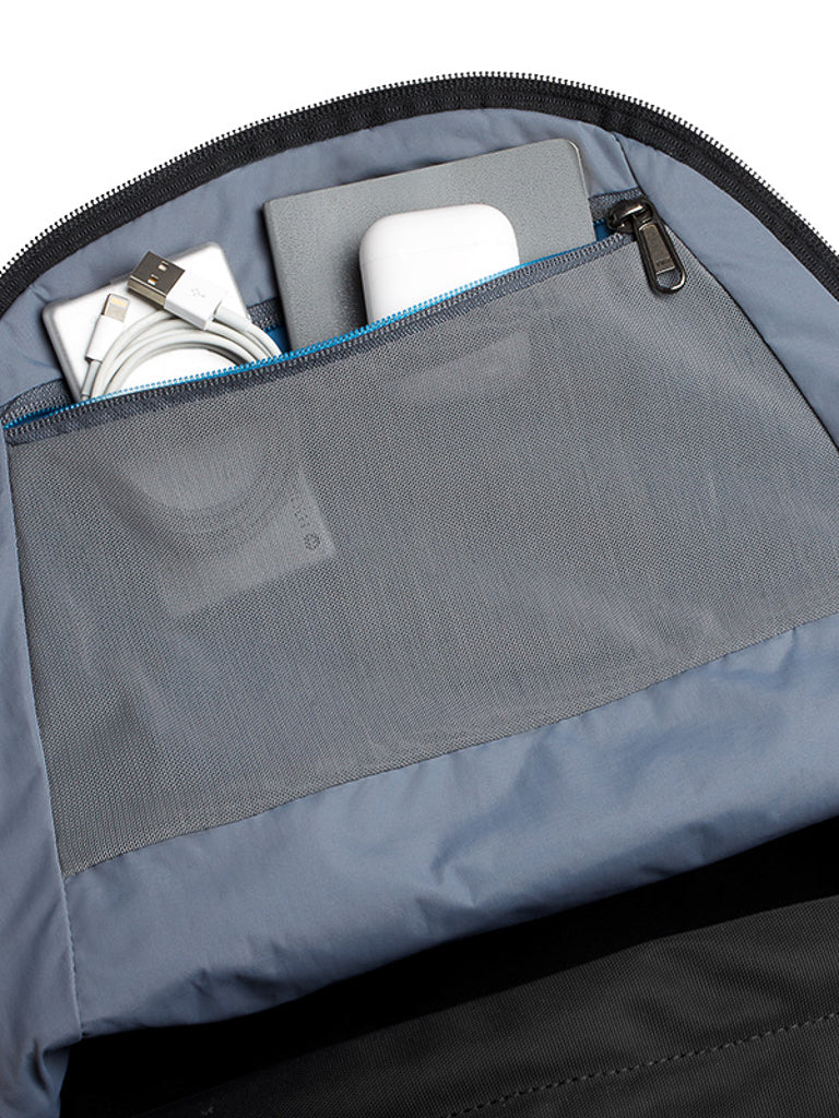 A close-up of the Bellroy Classic Backpack - 20L’s interior shows a charging cable, white adapter, and gray device neatly organized in a mesh zip pocket—all crafted from recycled materials.