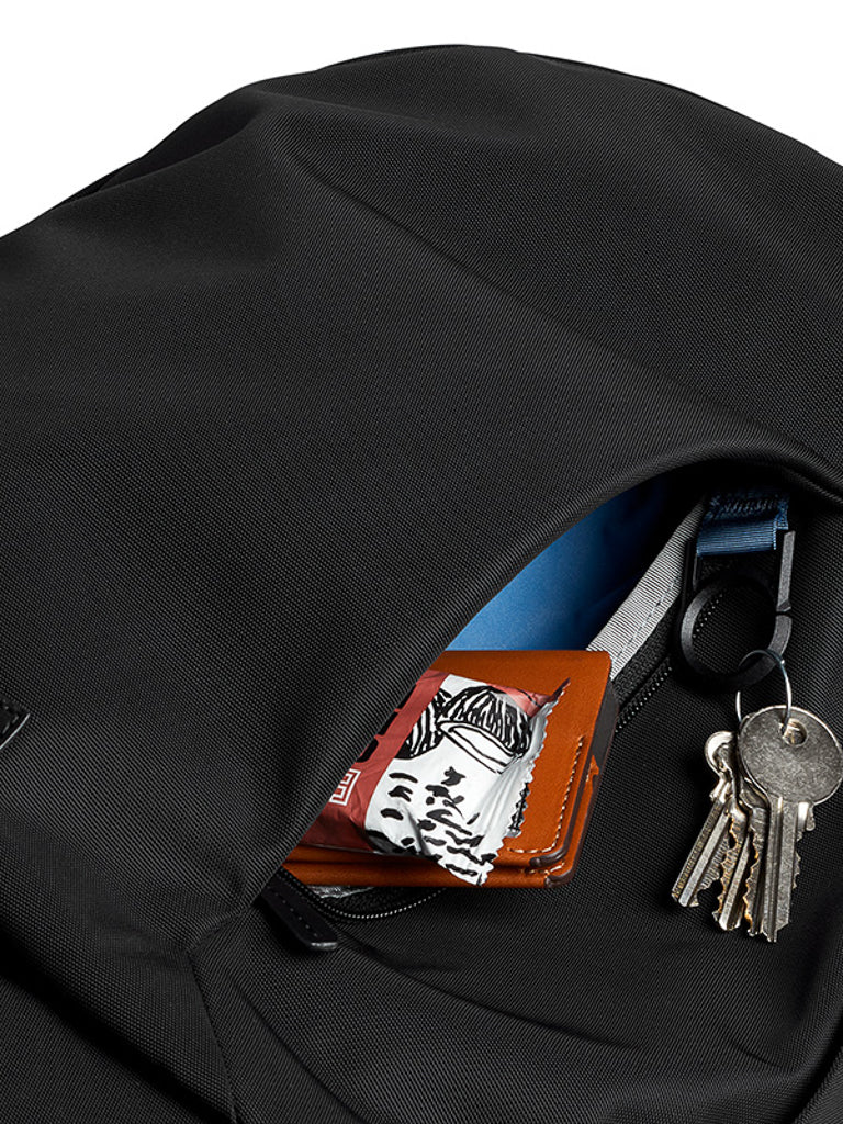 A close-up of the Bellroy Classic Backpack - 20L’s open pocket shows a wallet, a black-and-white packet, and keys on a zipper pull—ideal for staying organized on your daily commute.