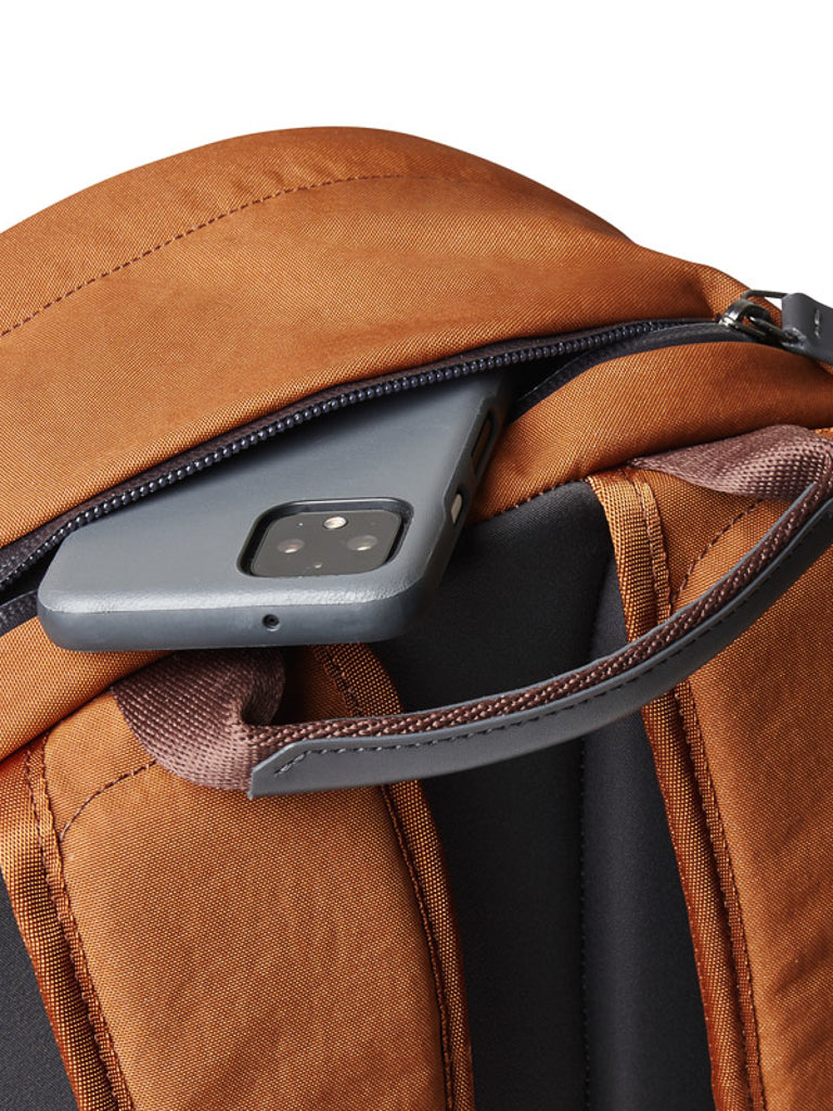 A close-up of the Bellroy Classic Backpack - 20L made from recycled materials shows a partially open zipper pocket with a smartphone in a gray case inside.